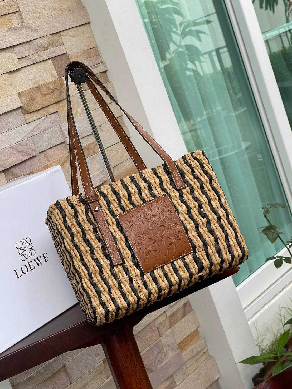LOEWE X PAULA'S IBIZA SMALL SQUARE BASKET BAG กระเป๋าสะพายไหล่จากโลเอเว่ เป็นกระเป๋าสานขึ้นจากใบกก (Reed) ที่มีทั้งความเหนียวและความยืดหยุ่น สวยน่ารักแบบมินิมอล มีความทนทานสูง ดูแลรักษาง่าย ด้านหน้าและหูเป็นหนังแท้(calf skin) ส่วนภายในมีถุงผ้าแบบหูรู