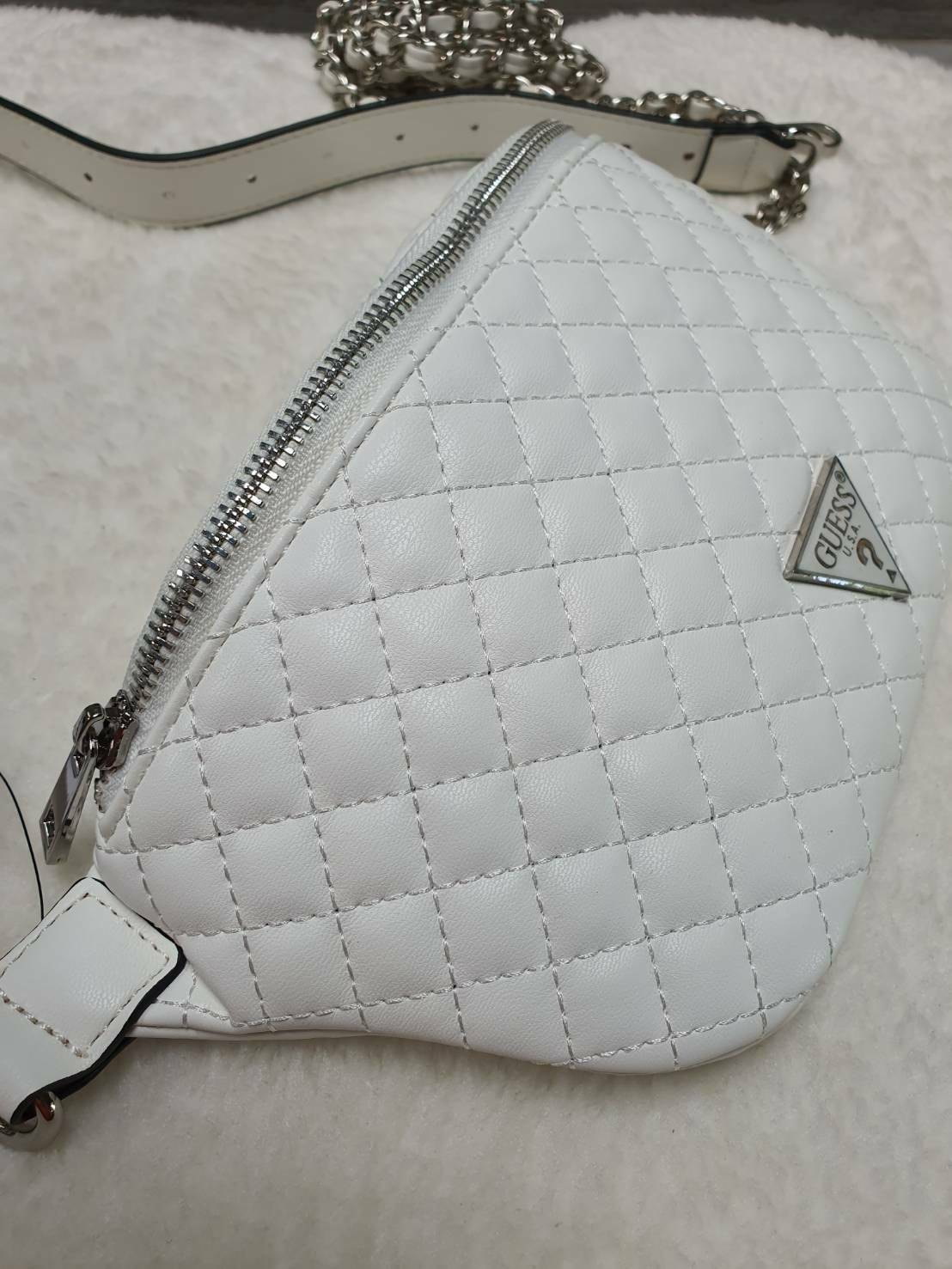 กระเป๋า Guess รุ่นนี้คาดเอว/คาดอก/สะพายข้างได้ครบทุกฟังก์ชั่น ด้านหน้าหนังเป็นลายตาราง ติดโลโก้แบรนด์รูปสามเหลี่ยมด้านหน้า เปิดปิดด้วยซิปยาว ด้านในเป็นช่องกว้างมีช่องซิปด้านใน ตัวกระเป๋าด้านหลังเป็นหนังเรียบ รุ่นนี้มีสายสะพายมา 2 เส้น เส้นแรกเป็นสายหนังปร