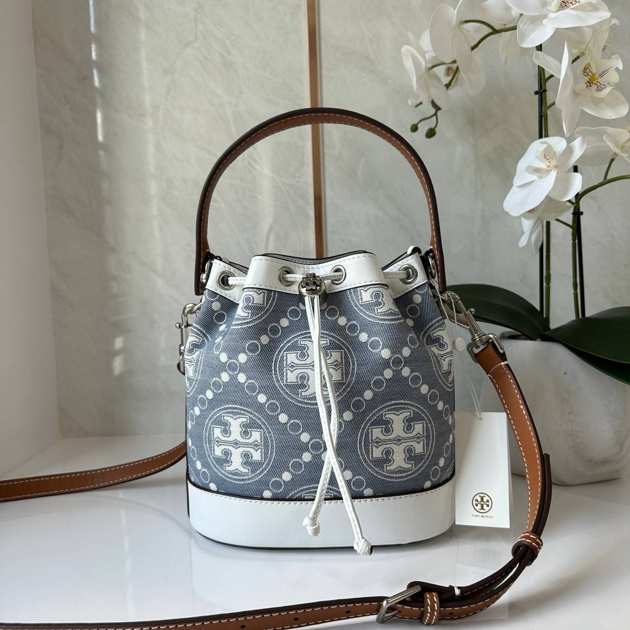 TORY BURCH T Monogram Denim Bucket Bag MEDIUM คอลเลคชั่นใหม่ รูปแบบคลาสสิค พกพาความหรูหราไปได้ทุกที่ด้วยกระเป๋าทรง Bucket ขนาดกลางและปิดด้วยเชือกรูดพร้อมโลโก้แวววาว วัสดุผ้าเดนิมแจ็คการ์ด ตัดขอบหนังแท้
