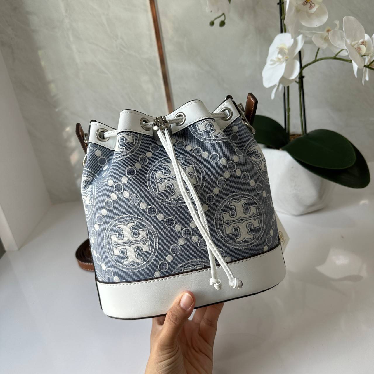 TORY BURCH T Monogram Denim Bucket Bag MEDIUM คอลเลคชั่นใหม่ รูปแบบคลาสสิค พกพาความหรูหราไปได้ทุกที่ด้วยกระเป๋าทรง Bucket ขนาดกลางและปิดด้วยเชือกรูดพร้อมโลโก้แวววาว วัสดุผ้าเดนิมแจ็คการ์ด ตัดขอบหนังแท้