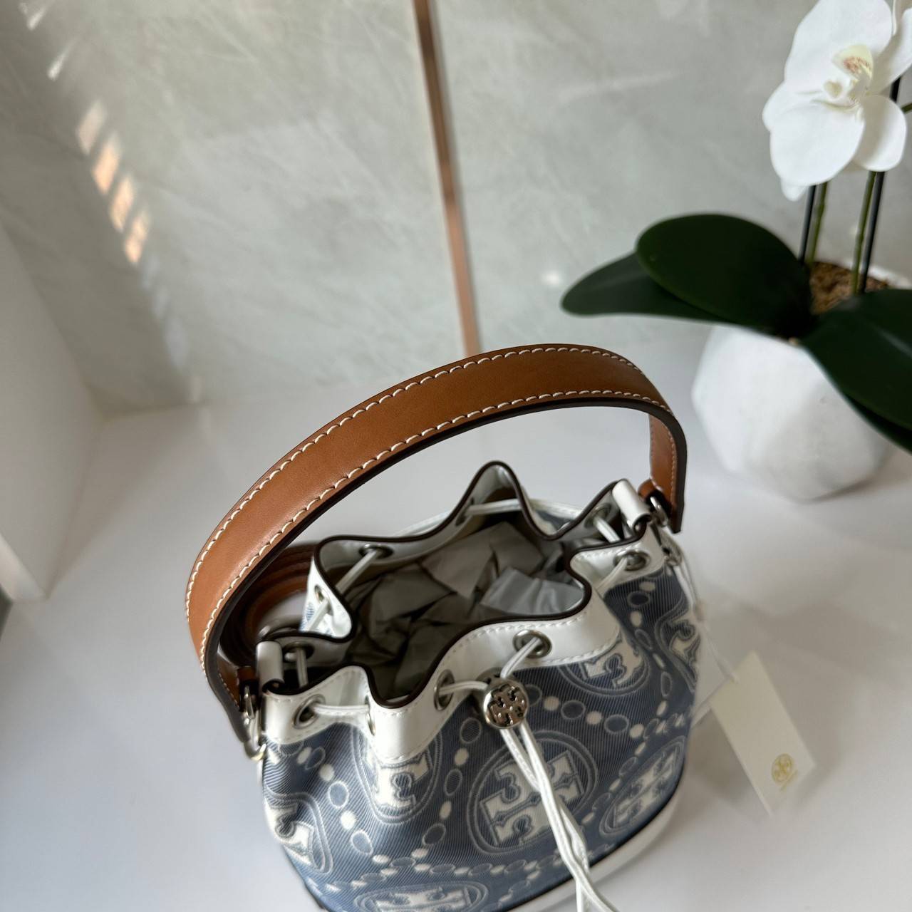 TORY BURCH T Monogram Denim Bucket Bag MEDIUM คอลเลคชั่นใหม่ รูปแบบคลาสสิค พกพาความหรูหราไปได้ทุกที่ด้วยกระเป๋าทรง Bucket ขนาดกลางและปิดด้วยเชือกรูดพร้อมโลโก้แวววาว วัสดุผ้าเดนิมแจ็คการ์ด ตัดขอบหนังแท้