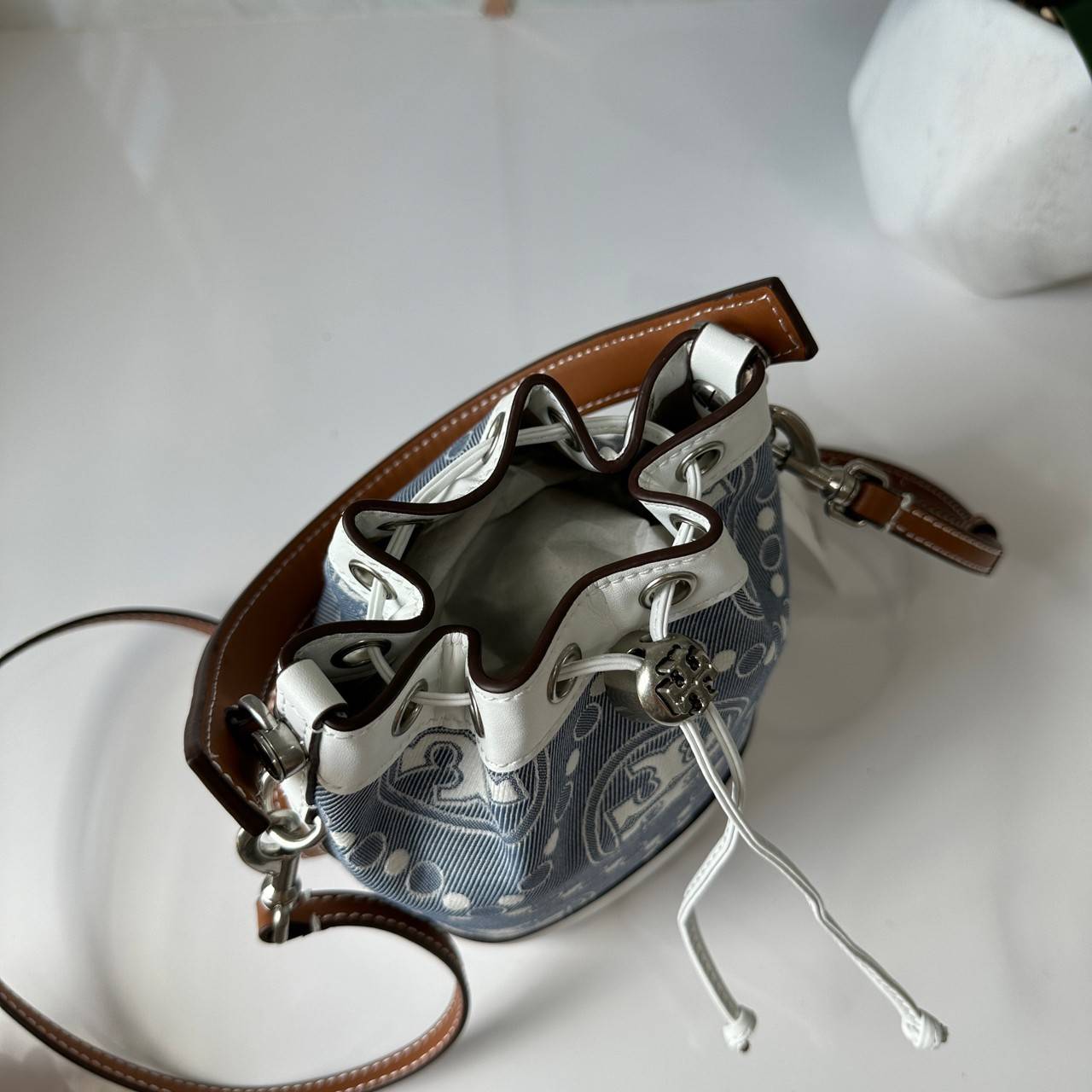 TORY BURCH Mini T Monogram Denim Bucket Bag คอลเลคชั่นใหม่ รูปแบบคลาสสิค พกพาความหรูหราไปได้ทุกที่ด้วยกระเป๋าทรง Bucket ขนาดกลางและปิดด้วยเชือกรูดพร้อมโลโก้แวววาว วัสดุผ้าเดนิมแจ็คการ์ด ตัดขอบหนังแท้ สวยหรู ทันสมัยสุดๆคะ