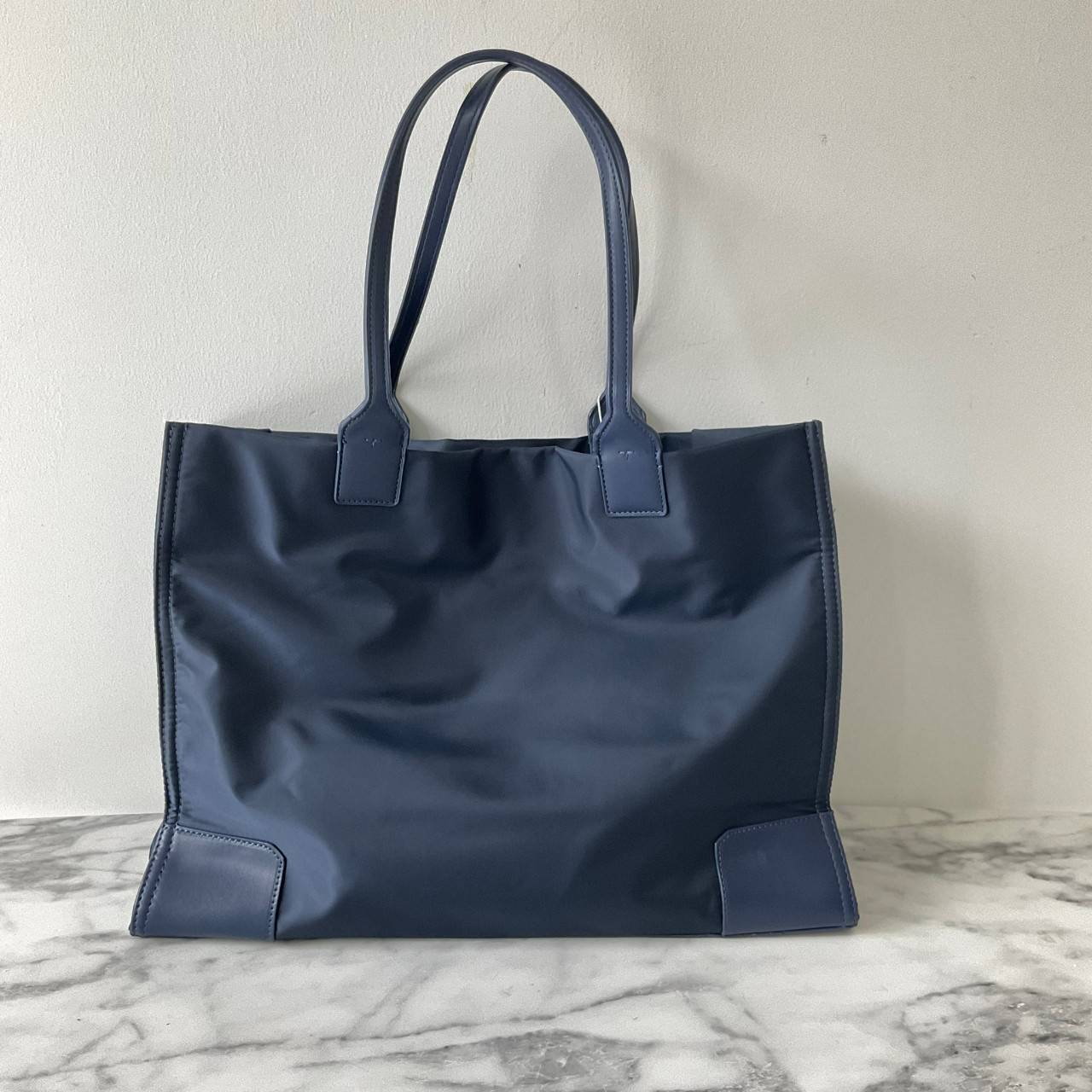 กระเป๋าทรงโท้ทใบใหญ่ TORY BURCH ELLA TOTE BAG วัสดุ NYLON ทั้งใบตัดด้วยหนังสีดำ แต่งโลโก้แบรนด์ด้านหน้า ด้านข้างมีกระดุม สามารถขยายทรงได้ ด้านในเปิดปิดด้วยกระดุมแม่เหล็กฝัง ช่องกว้างหลักหนึ่งช่องและช่องซิปอีกช่อง สามารถใส่แล็ปท็อปได้สบาย ใบใหญ่เว่อวัง ไอเ