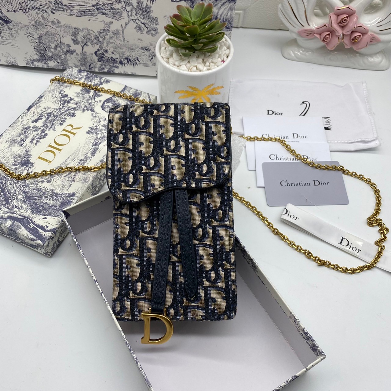 หนังแท้ DIOR PHONE BAG / DIOR PHONE HOLDER BAG กระเป๋าใส่โทรศัพท์เอกลักษณ์ของความหรู สายสะพายโซ่อะไหล่ทอง วัสดุหนังแท้และผ้า Jacquard อย่างดีสวยงามที่สุด ผสมผสานความสง่างามและคลาสสิกที่เข้ากับยุคสมัย ด้านหน้าโดดเด่นด้วยซิกเนเจอร์แบรนด์ เป็นอีกหนึ่งรุ่นที่