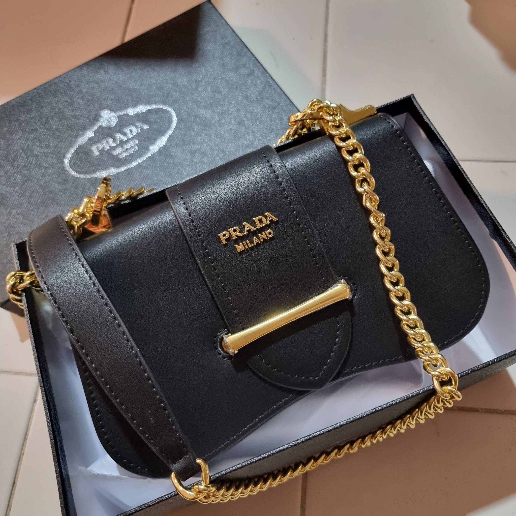 PRADA FRAGRANCE SHOULDER BAG WITH GWP ไอเท็มสุดโปรดที่ควรค่าแก่การครอบครองและเก็บสะสม กระเป๋าสะพายไหล่ สวยคม สีดำคลาสสิคตัดกับอะไหล่ทองเป็นอย่างดี วัสดุหนังแท้เต็มใบ เปิดปิดด้วยแถบหนังสอดในช่อง ใช้งานสะดวก พกพาง่าย ขนาดกำลังสวย สายสะพายในตัว สะพายได้หลากห
