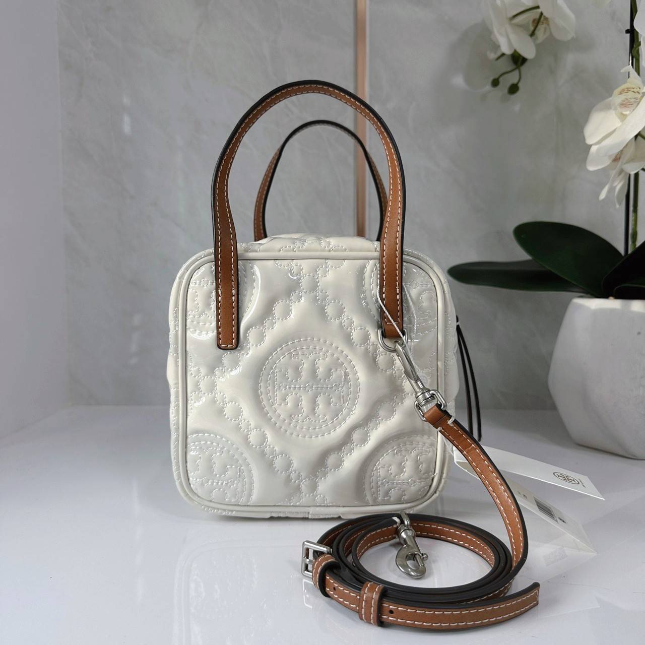Tory Burch T Monogram Embroidered Patent Cube คอลเลคชั่นใหม่ รุ่นลิมิเต็ดรูปทรงใหม่ T Monogram สุดcube วัสดุหนังแท้ เปิด-ปิดด้วยซิป ภายในกว้าง มีช่องแยก 1 ช่อง สามารถใส่โทรศัพท์มือถือได้ทุกรุ่น สามารถถือหิ้วหรือสะพายได้ สายสามารถถอดและปรับระดับได้คะ