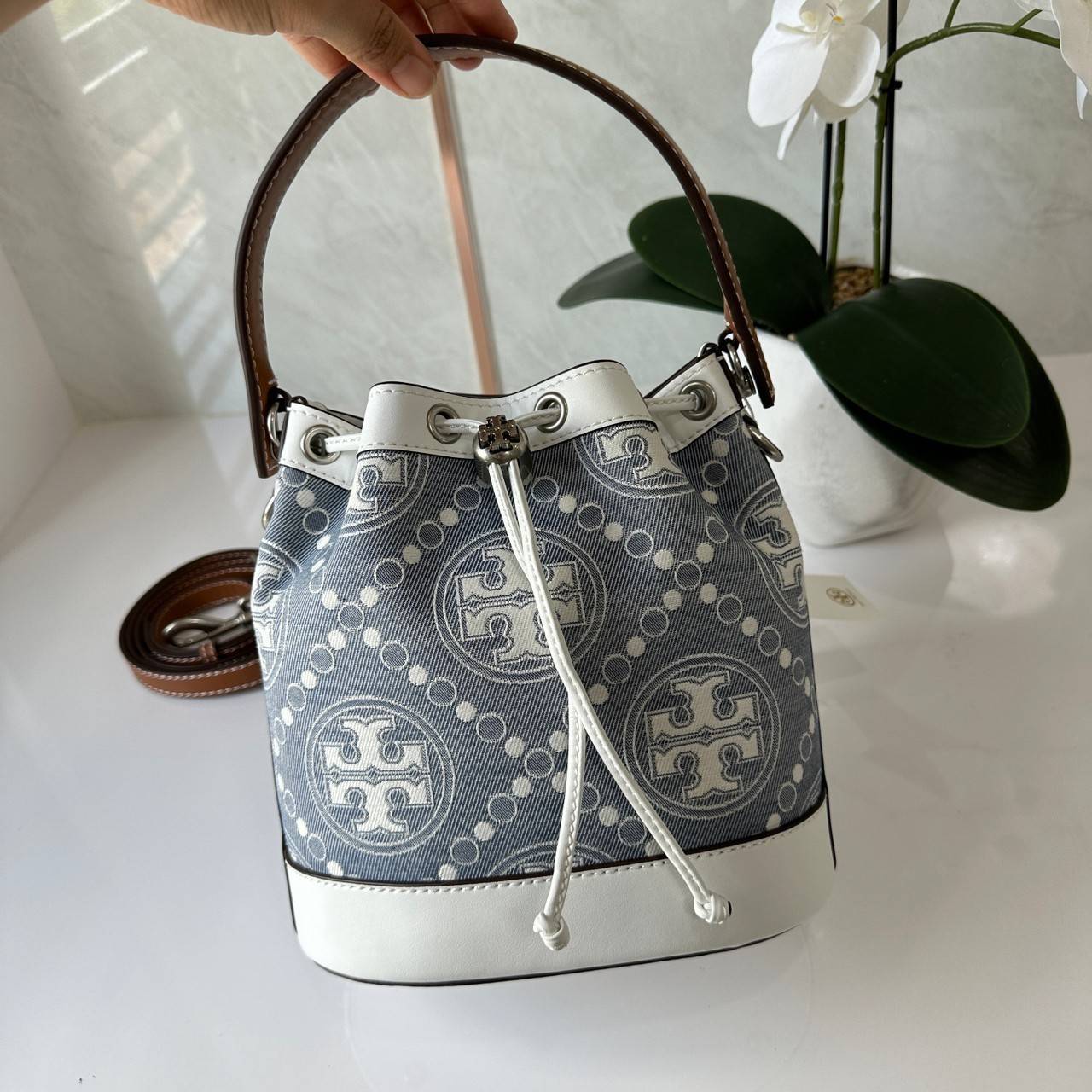 TORY BURCH T Monogram Denim Bucket Bag MEDIUM คอลเลคชั่นใหม่ รูปแบบคลาสสิค พกพาความหรูหราไปได้ทุกที่ด้วยกระเป๋าทรง Bucket ขนาดกลางและปิดด้วยเชือกรูดพร้อมโลโก้แวววาว วัสดุผ้าเดนิมแจ็คการ์ด ตัดขอบหนังแท้