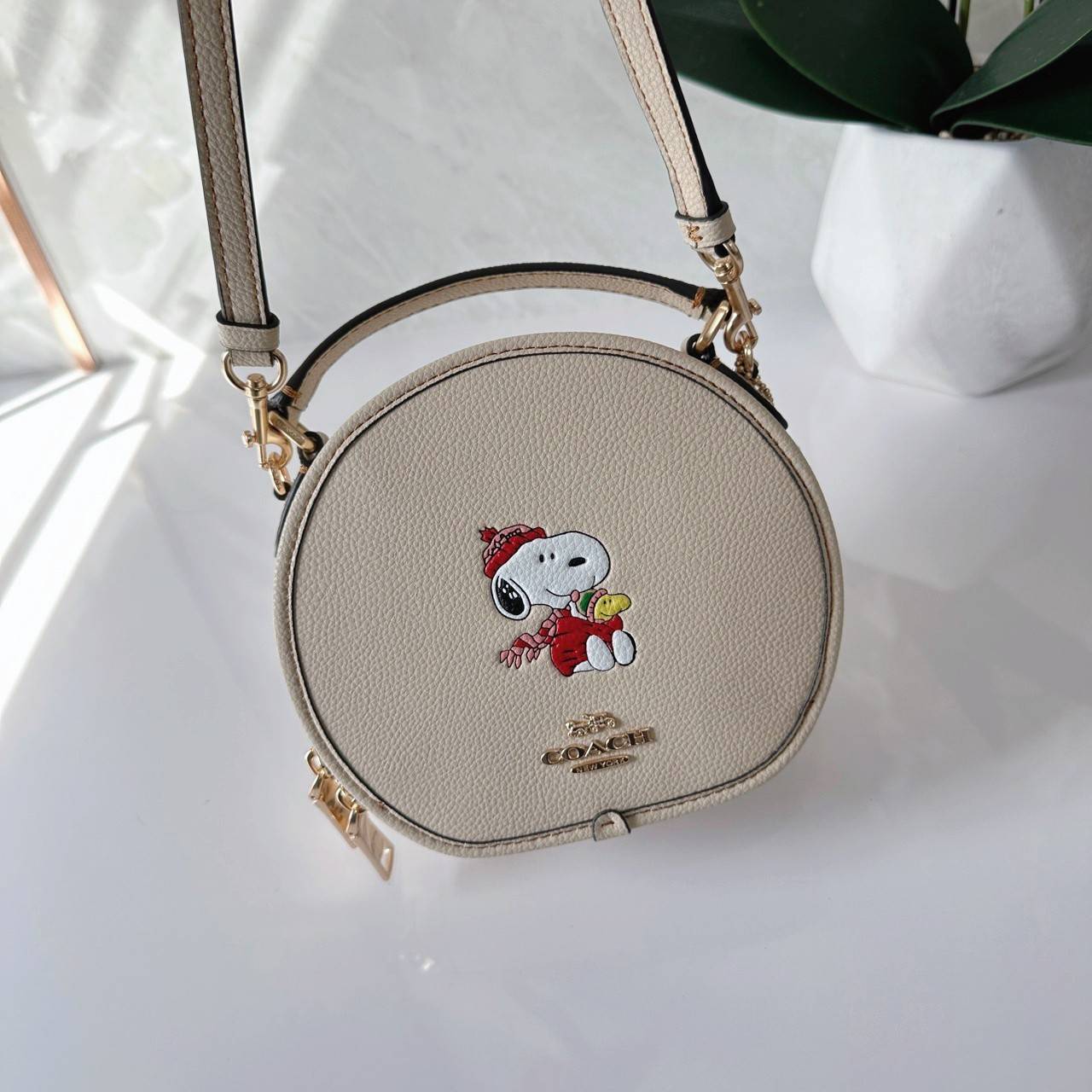 COACH X PEANUTS CANTEEN CROSSBODY WITH SNOOPY PRESENT MOTIF (CE845,CF290) กระเป๋าสะพายข้างทรงกลมไซส์มินิ มีหูจับ วัสหนังแท้ ด้านหน้าโดดเด่นด้วยรูปการ์ตูนSnoopy