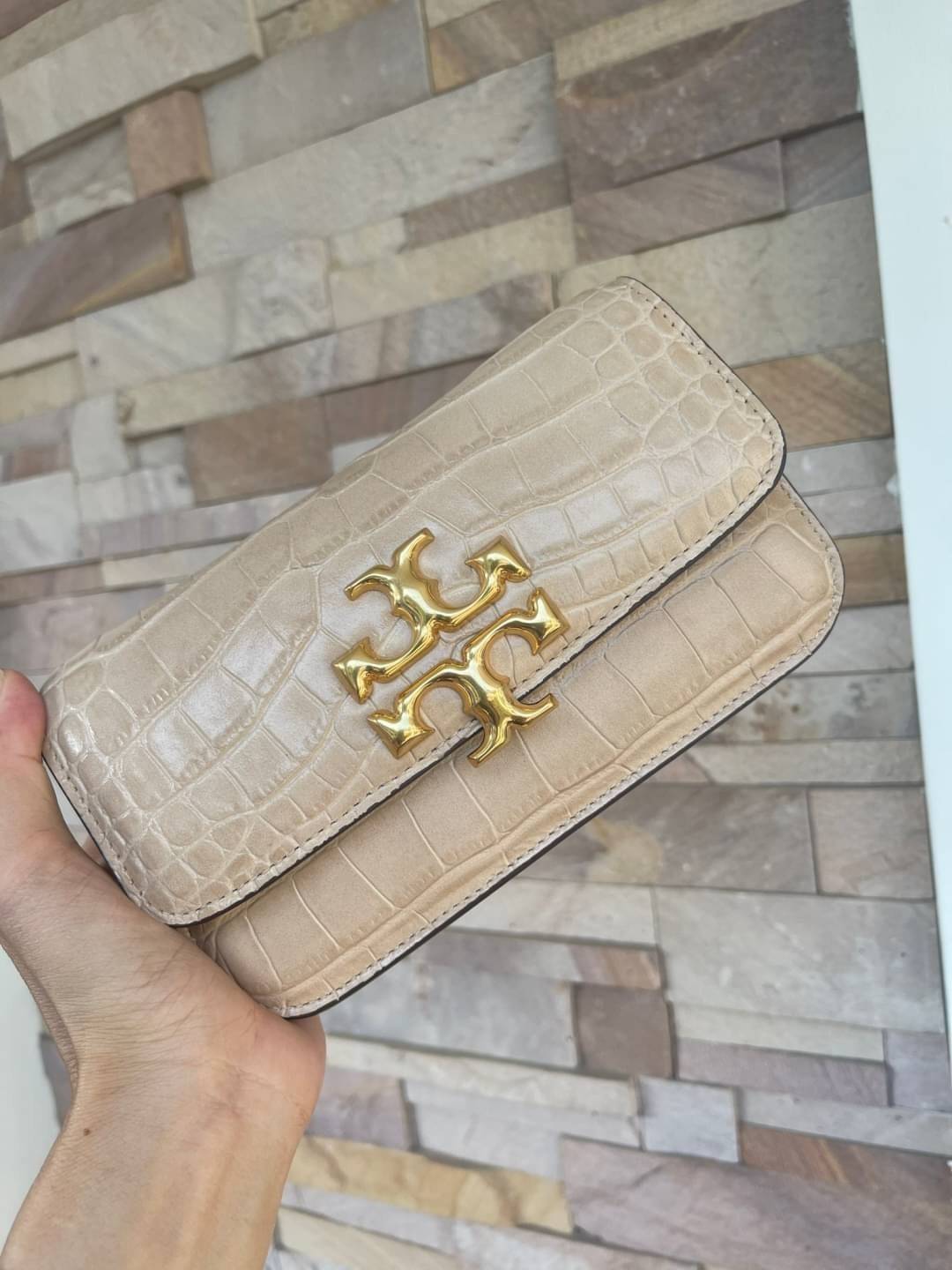 Tory Burch Eleanor Crocodile-Embossed Phone Crossbody Bag จุดเด่นของรุ่นนี้คือดีไซน์ออกมาในสไตล์คลาสสิกที่มาพร้อมกับฮาร์ดแวร์ที่ทำจากวัสดุทองเหลืองและสายสะพายโซ่เกลียวสีทอง ซึ่งการออกแบบได้รับแรงบันดาลใจมาจากเครื่องประดับ รูปทรงกะทัดรัดจึงสามารถสะพายใช้งา