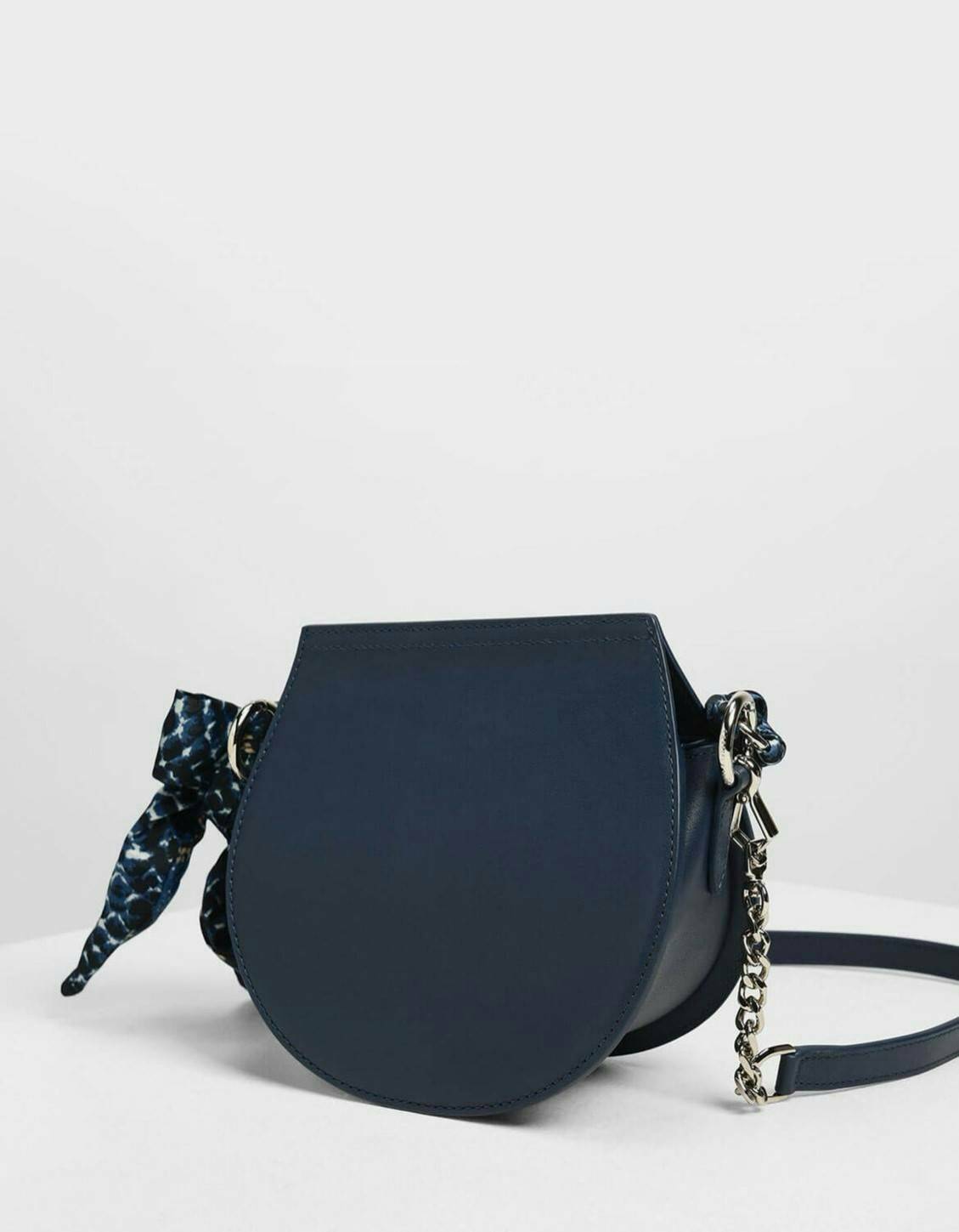 CHARLES & KEITH รุ่น LEATHER SATIN SCARF CROSSBODY BAG SL2-50150828 ราคาปกติช้อป ( ฿3,590.00 ) กระเป๋าถือ และ สะพาย ทรงโค้งมน หนังเรียบ ตั้งอยู่ทรง ด้านหน้าติดโลโก้แบรนด์ อะไหล่เงิน หูจับสายกระเป๋าร้อยเข้ากับห่วงเหล็กกลมๆ ด้วยผ้าลายสวยงามผูกเป็นโบว์เก๋ๆ ถ