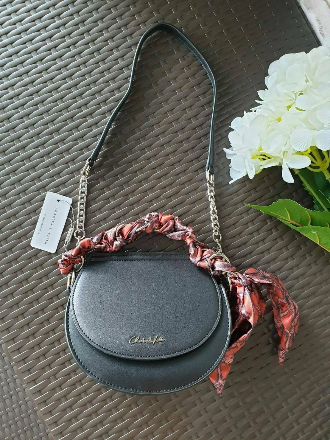 CHARLES & KEITH รุ่น LEATHER SATIN SCARF CROSSBODY BAG SL2-50150828 ราคาปกติช้อป ( ฿3,590.00 ) กระเป๋าถือ และ สะพาย ทรงโค้งมน หนังเรียบ ตั้งอยู่ทรง ด้านหน้าติดโลโก้แบรนด์ อะไหล่เงิน หูจับสายกระเป๋าร้อยเข้ากับห่วงเหล็กกลมๆ ด้วยผ้าลายสวยงามผูกเป็นโบว์เก๋ๆ ถ