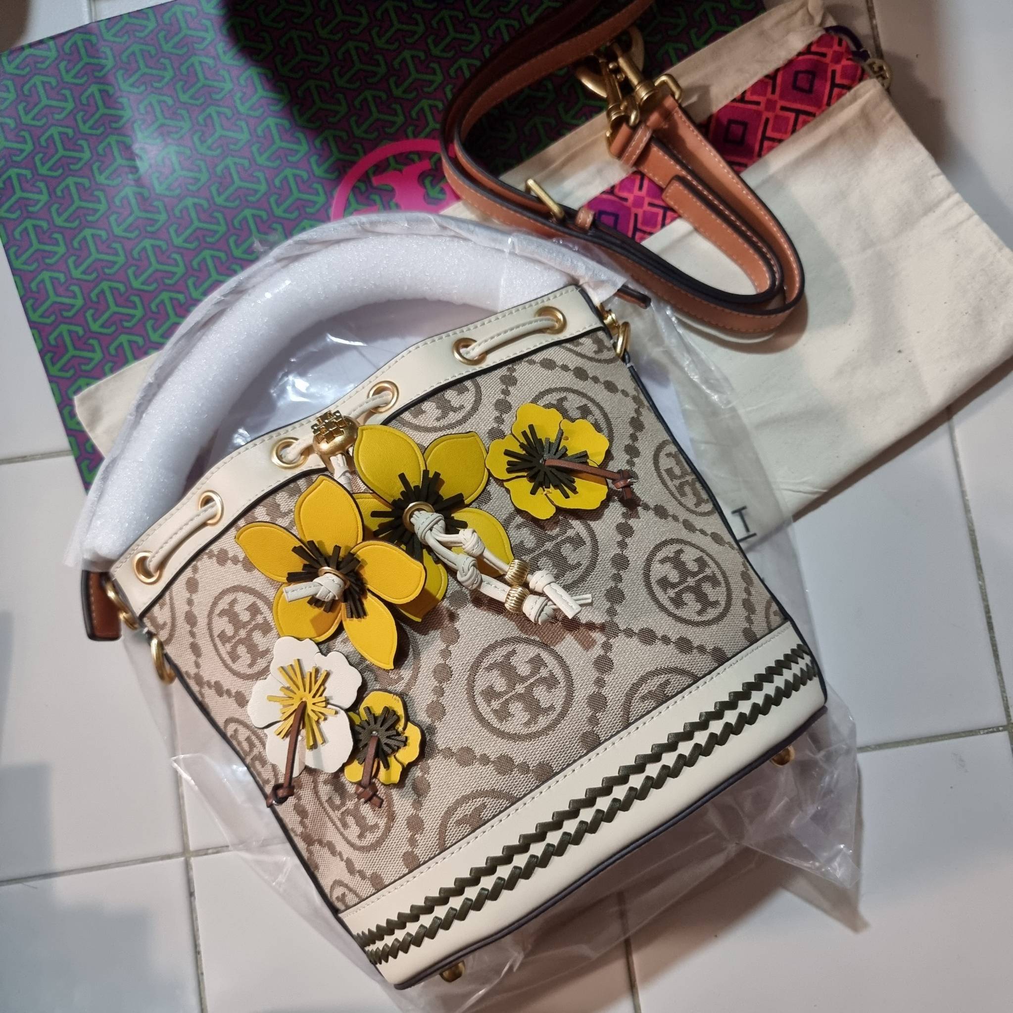 TORY BURCH T MONOGRAM FLORAL BUCKET BAG คอลเลคชั่นใหม่ พร้อมเสิร์ฟความสวยให้ถึงบ้าน!! กระเป๋าบัคเก็ตทรงยอดนิยม ดีไซน์ใหม่ล่าสุด สไตล์งานคราฟ มีลูกเล่นประดับดอกไม้กับตัวกระเป๋า และตัวรูดสาย วัสดุผ้า jacquard ตัดสลับหนังแท้ หูจับและขอบกระเป๋าตกแต่งลายสานสวย