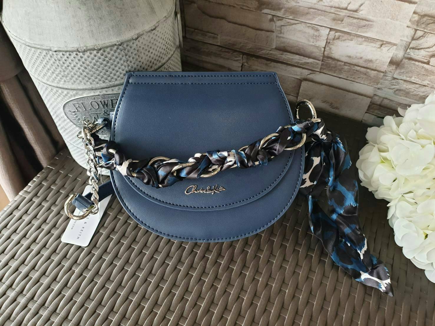 CHARLES & KEITH รุ่น LEATHER SATIN SCARF CROSSBODY BAG SL2-50150828 ราคาปกติช้อป ( ฿3,590.00 ) กระเป๋าถือ และ สะพาย ทรงโค้งมน หนังเรียบ ตั้งอยู่ทรง ด้านหน้าติดโลโก้แบรนด์ อะไหล่เงิน หูจับสายกระเป๋าร้อยเข้ากับห่วงเหล็กกลมๆ ด้วยผ้าลายสวยงามผูกเป็นโบว์เก๋ๆ ถ