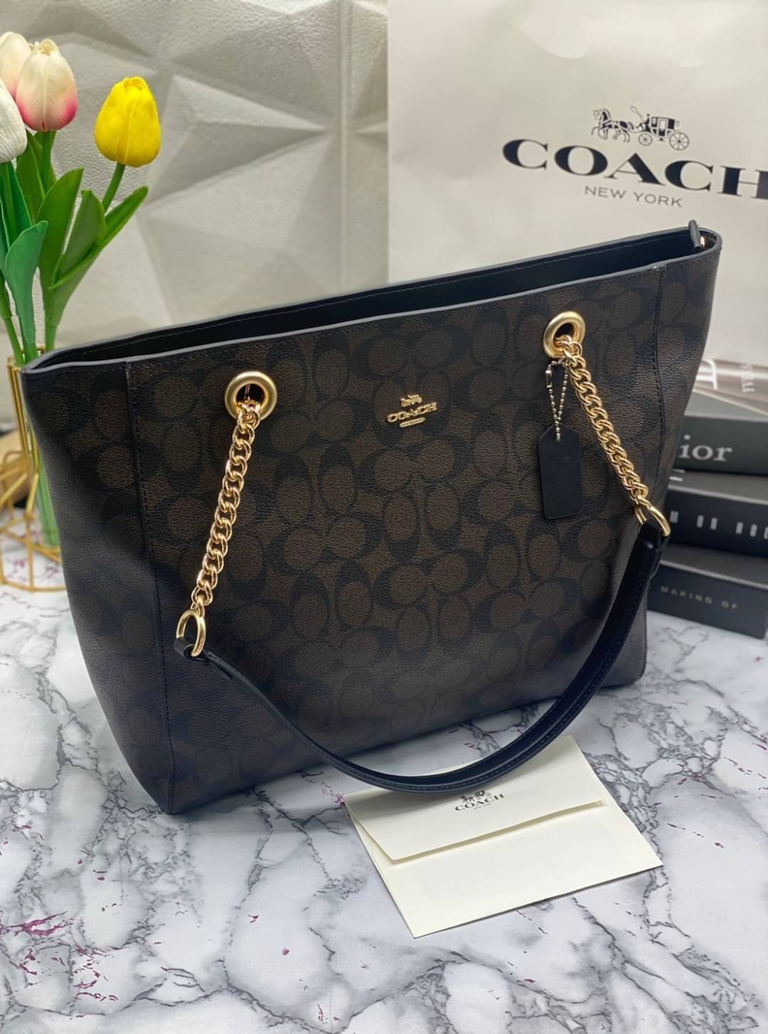 COACH Tote in Signature Canvas Bag กระเป๋าสะพายทรงช้อปปิ้ง สายกระเป๋าเป็นหนังสลับโซ่ทองสวยงาม เพิ่มความหรูหรา ภายในโล่งกว้างใส่ของได้เยอะมาก วัสดุ Canvas เคลือบลายซิกเนเจอร์และหนัง พร้อมซิปกลางเก็บของได้มิดชิดเลยค่ะ มี 3 สี น้ำตาล ดำ ขาว