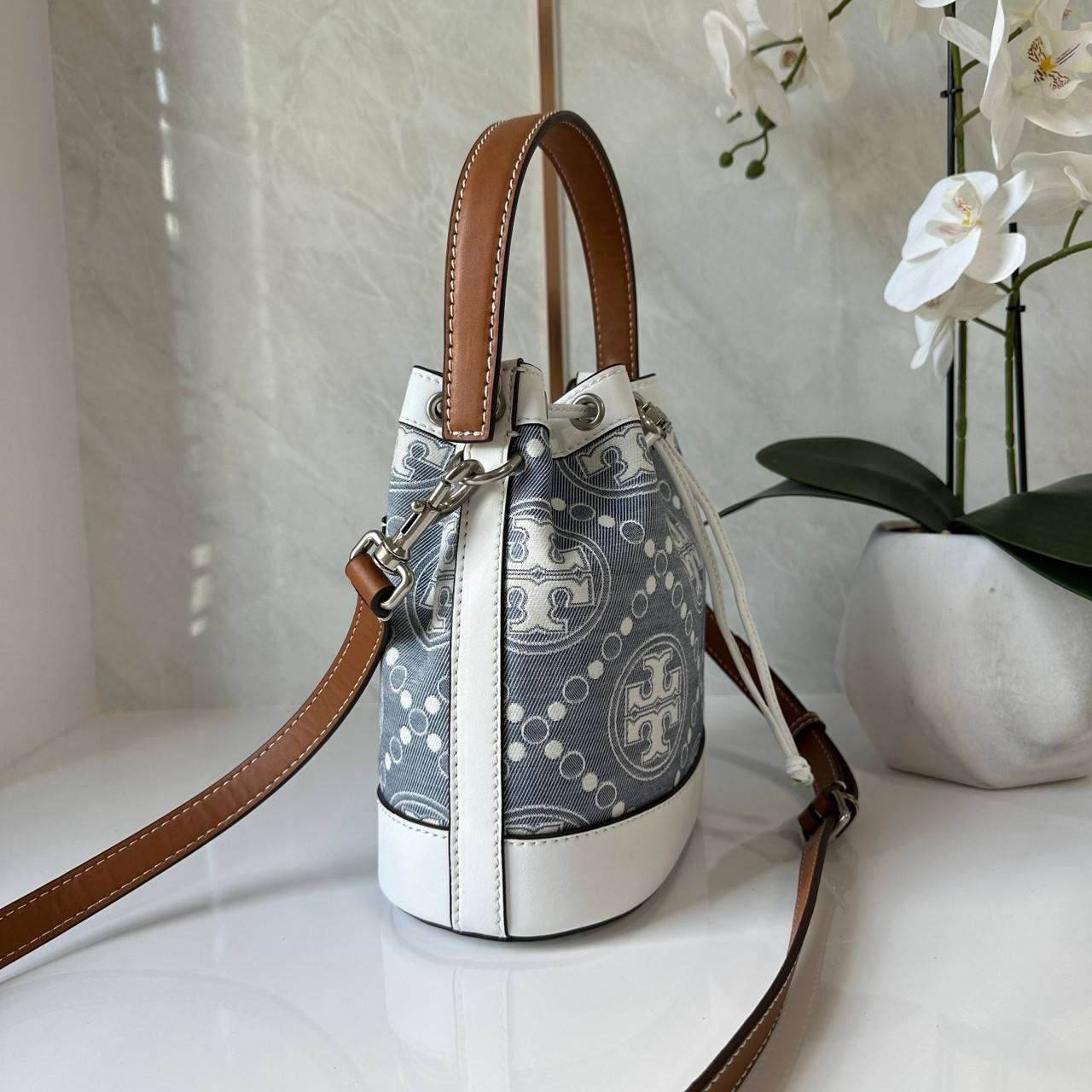 TORY BURCH T Monogram Denim Bucket Bag MEDIUM คอลเลคชั่นใหม่ รูปแบบคลาสสิค พกพาความหรูหราไปได้ทุกที่ด้วยกระเป๋าทรง Bucket ขนาดกลางและปิดด้วยเชือกรูดพร้อมโลโก้แวววาว วัสดุผ้าเดนิมแจ็คการ์ด ตัดขอบหนังแท้