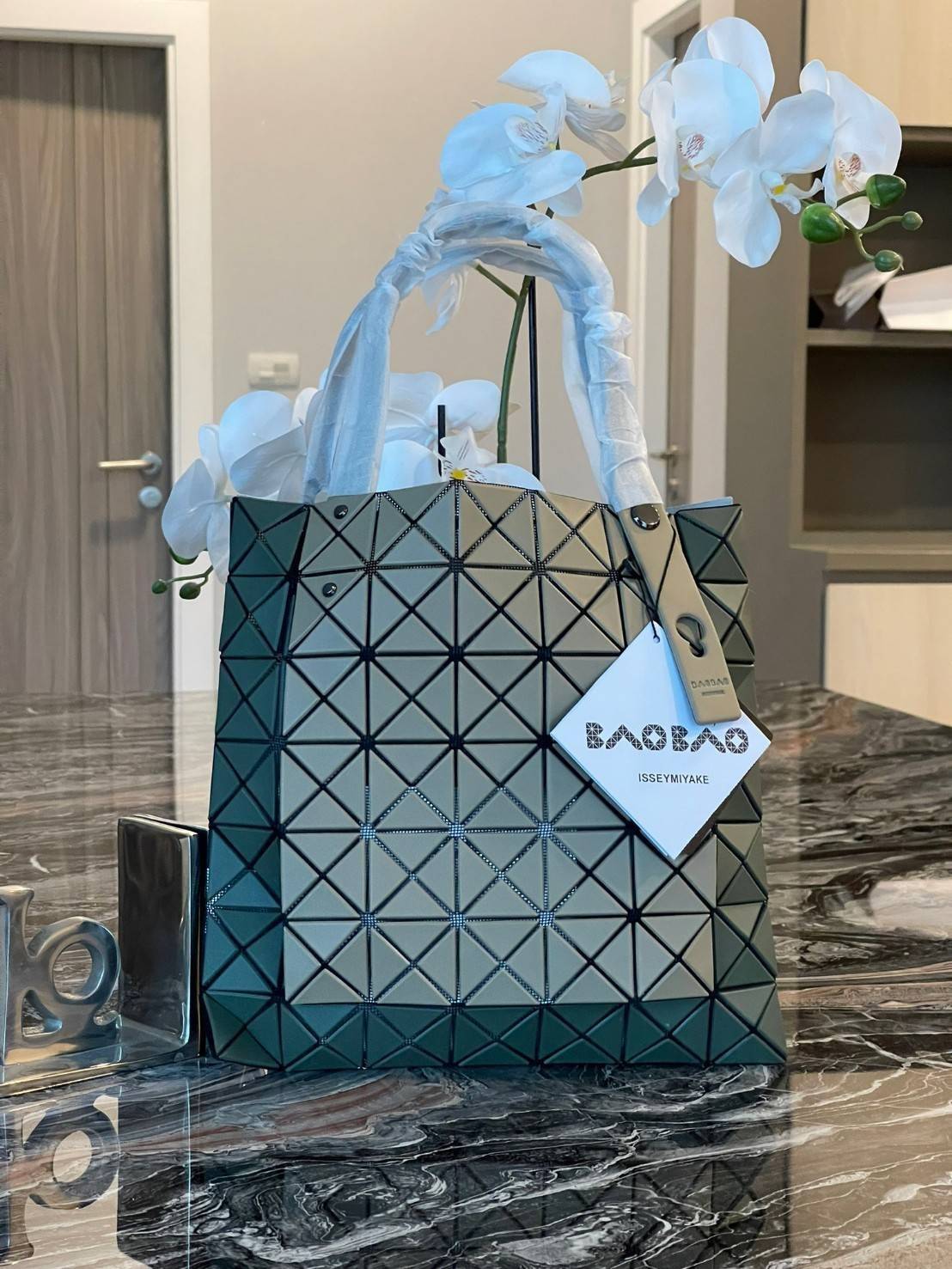 Baobao Issey Miyake Prism Kangaroo tote bag กระเป๋าถือทรงโท้ทที่ประดิษฐ์ขึ้นอย่างเชี่ยวชาญในญี่ปุ่น มาพร้อมแผงเรขาคณิตสำหรับการออกแบบที่ได้รับแรงบันดาลใจจากกระดาษพับ ซิลลูเอทอันเป็นเอกลักษณ์นี้ปิดท้ายด้วยสายรัดแบบอสมมาตร มีการพัฒนาโครงสร้างทรงสามเหลี่ยมเพ