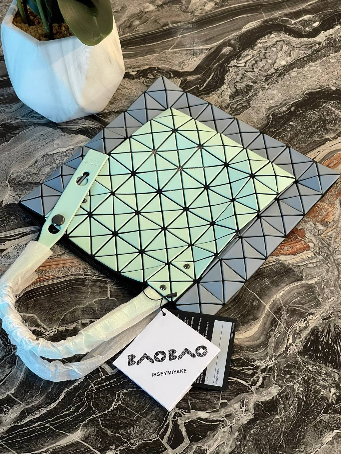 Baobao Issey Miyake Prism Kangaroo tote bag กระเป๋าถือทรงโท้ทที่ประดิษฐ์ขึ้นอย่างเชี่ยวชาญในญี่ปุ่น มาพร้อมแผงเรขาคณิตสำหรับการออกแบบที่ได้รับแรงบันดาลใจจากกระดาษพับ ซิลลูเอทอันเป็นเอกลักษณ์นี้ปิดท้ายด้วยสายรัดแบบอสมมาตร มีการพัฒนาโครงสร้างทรงสามเหลี่ยมเพ