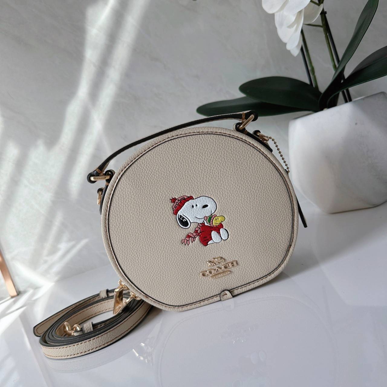 COACH X PEANUTS CANTEEN CROSSBODY WITH SNOOPY PRESENT MOTIF (CE845,CF290) กระเป๋าสะพายข้างทรงกลมไซส์มินิ มีหูจับ วัสหนังแท้ ด้านหน้าโดดเด่นด้วยรูปการ์ตูนSnoopy