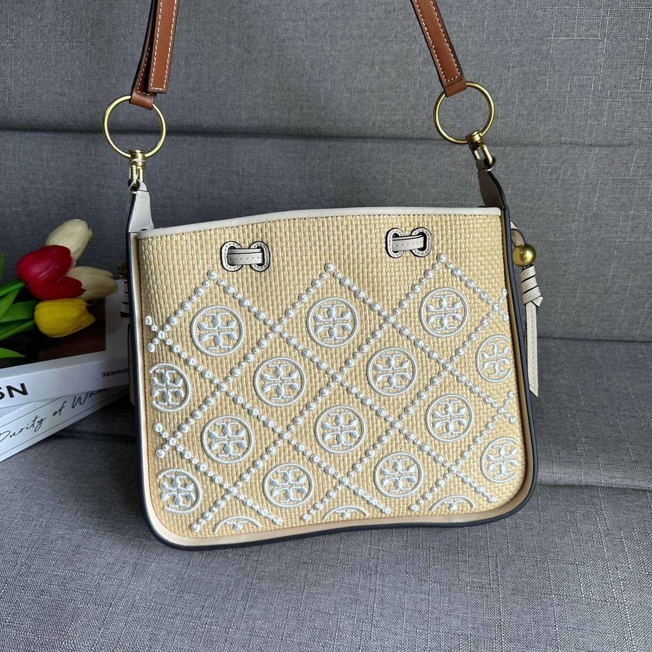 TORY BURCH T Monogram Straw Bell Bag กระเป๋าสะพายข้างรุ่นคลาสสิกที่ได้แรงบันดาลใจจากการควิลท์แบบดั้งเดิมของเพนซิลเวเนีย คอลเลกชันบ่งบอกถึงความมีสไตล์เหนือกาลเวลา รูปทรงเรียวโดดเด่น ปักทอลายแบรนด์อย่างสวยงาม เปิด ปิดด้วยเชือกรูด ด้านในช่องโล่งกว้าง ซับในผ้