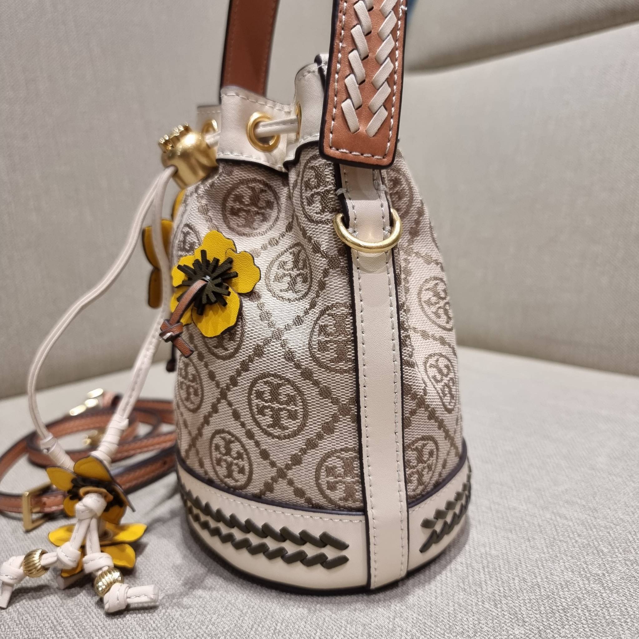 TORY BURCH MINI T MONOGRAM FLORAL BUCKET BAG คอลเลคชั่นใหม่ พร้อมเสิร์ฟความสวยให้ถึงบ้าน!! กระเป๋าบัคเก็ตทรงยอดนิยม ไซส์มินิ ดีไซน์ใหม่ล่าสุด สไตล์งานคราฟ มีลูกเล่นประดับดอกไม้กับตัวกระเป๋า และตัวรูดสาย วัสดุผ้า jacquard ตัดสลับหนังแท้ หูจับและขอบกระเป๋าต