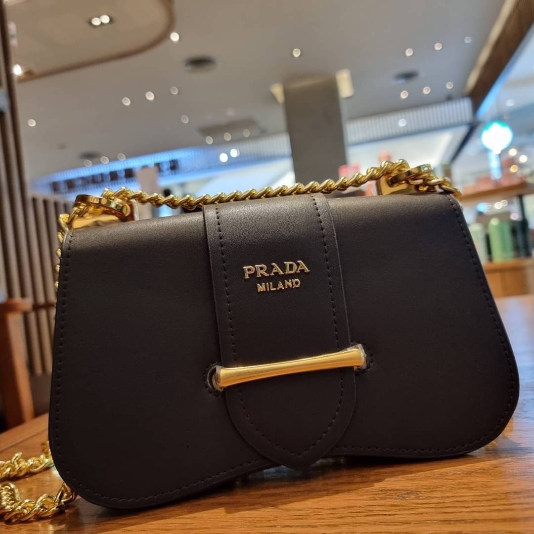 PRADA FRAGRANCE SHOULDER BAG WITH GWP ไอเท็มสุดโปรดที่ควรค่าแก่การครอบครองและเก็บสะสม กระเป๋าสะพายไหล่ สวยคม สีดำคลาสสิคตัดกับอะไหล่ทองเป็นอย่างดี วัสดุหนังแท้เต็มใบ เปิดปิดด้วยแถบหนังสอดในช่อง ใช้งานสะดวก พกพาง่าย ขนาดกำลังสวย สายสะพายในตัว สะพายได้หลากห
