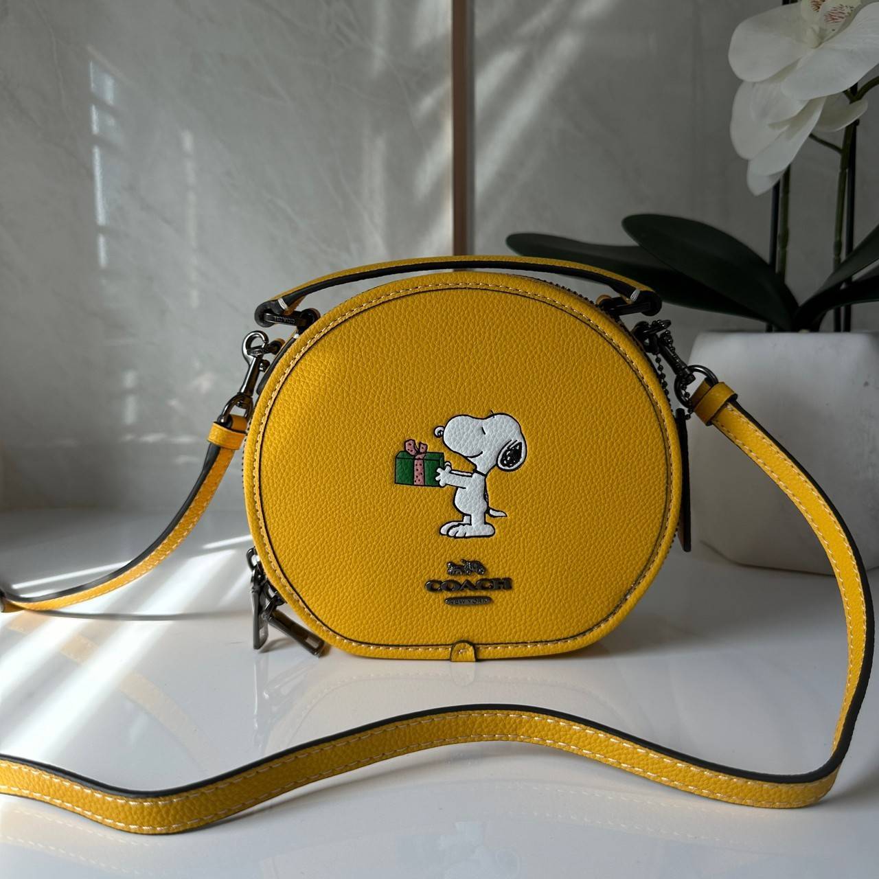 COACH X PEANUTS CANTEEN CROSSBODY WITH SNOOPY PRESENT MOTIF (CE845,CF290) กระเป๋าสะพายข้างทรงกลมไซส์มินิ มีหูจับ วัสหนังแท้ ด้านหน้าโดดเด่นด้วยรูปการ์ตูนSnoopy
