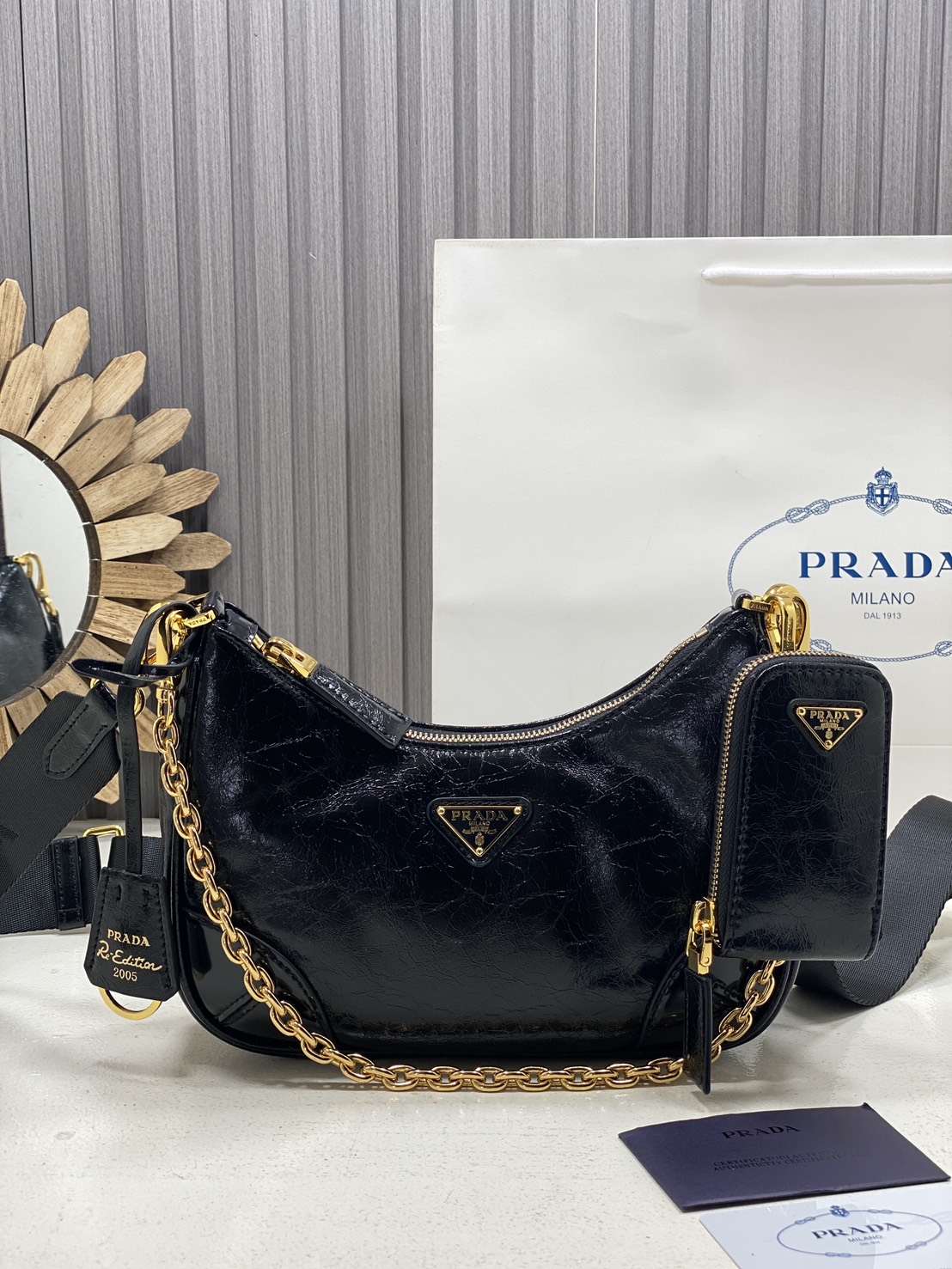 ORI หนังแท้ | Prada Re-Edition 2005 bag in Naplak leather กระเป๋าสะพายทรงโฮโบหนังแก้ว ดีไซน์เอฟเฟกต์มันวาวและเท็กซ์เจอร์ที่มีเสน่ห์สไตล์วินเทจ พร้อมทริกห้อยเพิ่มสไตล์สัมผัสที่โดดเด่นและร่วมสมัยยิ่งขึ้น