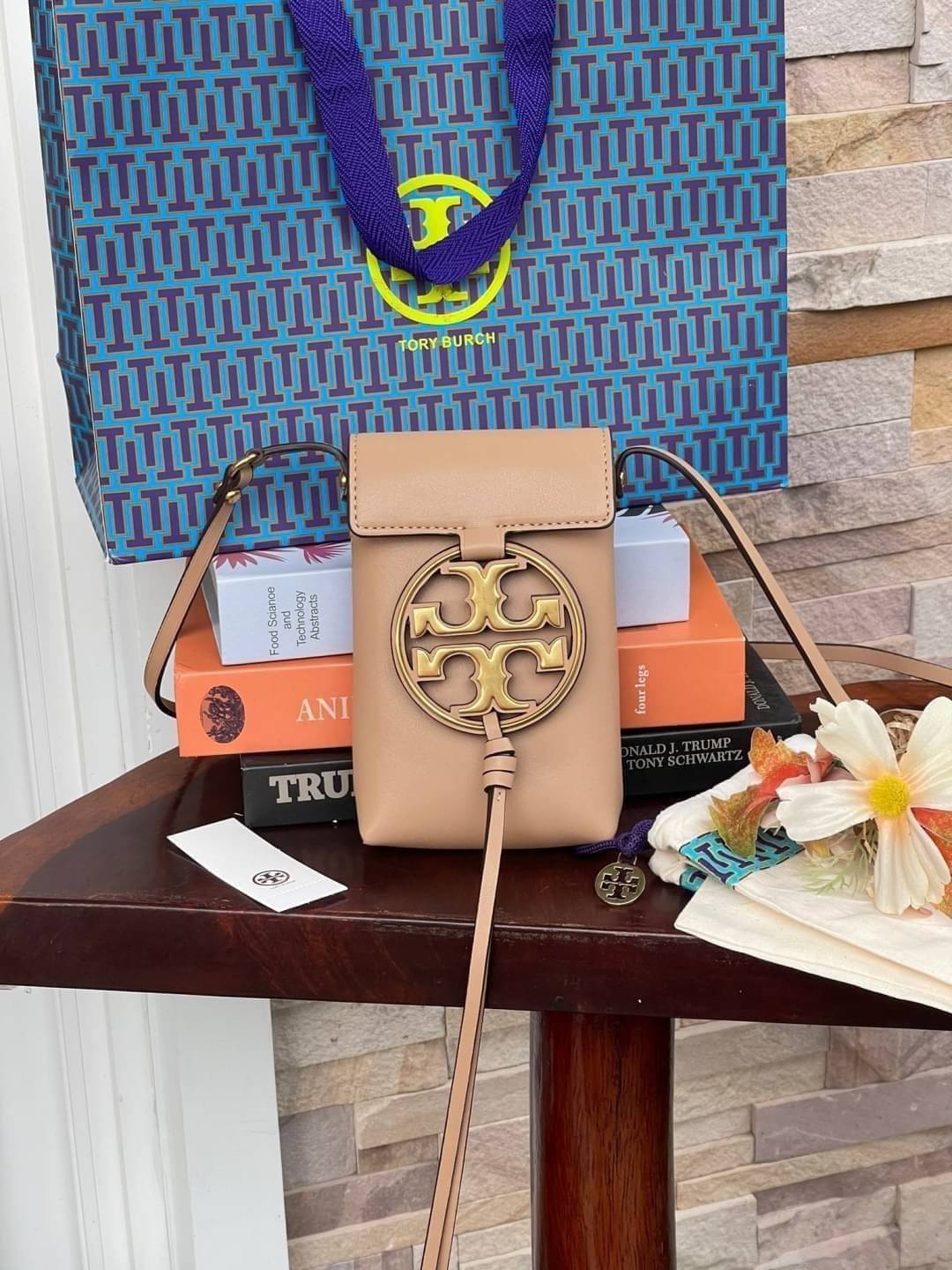 TORY BURCH MILLER METAL PHONE CROSSBODY อีกหนึ่งกระเป๋าใส่มือถือรุ่นฮิตที่เชื่อว่าหลาย ๆ คนต้องเคยเห็นผ่าน ๆ ตามาอย่างแน่นอน กับแบรนด์ Tory Burch ดีไซน์กระเป๋าทรงฝาพับแม่เหล็กใช้งานง่าย มาพร้อมดีเทล Logo แบรนด์โดดเด่นสีทองตัดกับหนังแกะสีดำ ดูหรูดูแพง! แต่