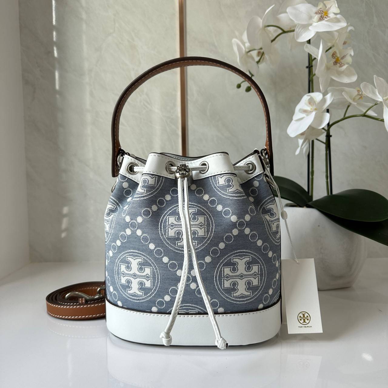 TORY BURCH T Monogram Denim Bucket Bag MEDIUM คอลเลคชั่นใหม่ รูปแบบคลาสสิค พกพาความหรูหราไปได้ทุกที่ด้วยกระเป๋าทรง Bucket ขนาดกลางและปิดด้วยเชือกรูดพร้อมโลโก้แวววาว วัสดุผ้าเดนิมแจ็คการ์ด ตัดขอบหนังแท้