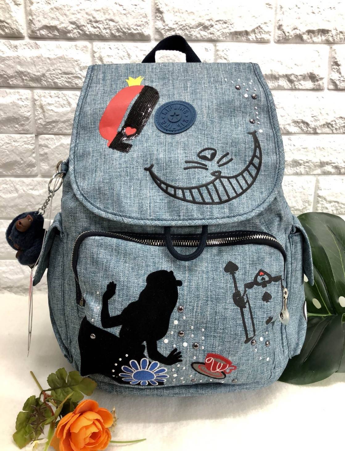 Kipling Disney's Alice in Wonderland Printed Backpack กระเป๋าเป้ Limited คอลเลคชั่น ALICE วัสดุ Denim+Polyester 100% เปิดปิดด้วยฝาปิด กระดุมแม่เหล็ก และซิปรอบ มาพร้อมพวงกุญเเจลิง ถอดเเยกใช้ได้ มีช่องซิปด้านหน้า และด้านหลัง พร้อมช่องใส่ของด้านข้าง 2 ด