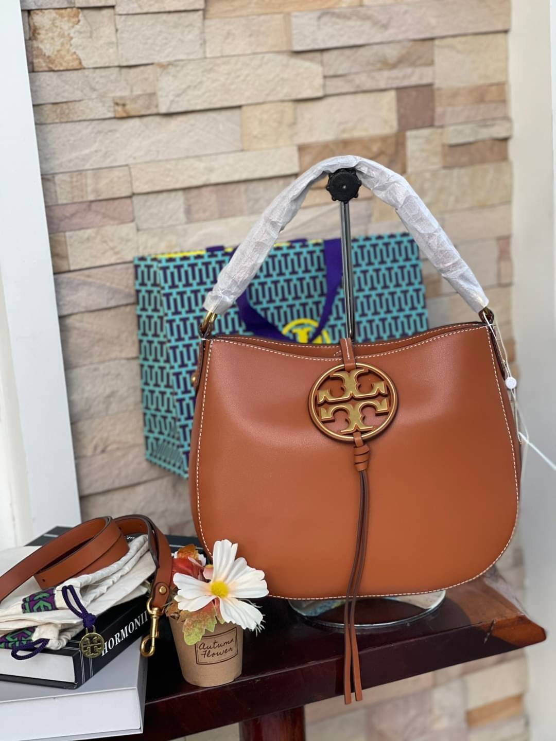 Tory burch miller metal-logo mini hobo bag มีกลิ่นอายสุดคลาสสิก ได้รับแรงบันดาลใจมาจากการขี่ม้า จึงได้ดีไซน์กระเป๋าออกมาในรูปแบบอานหลังม้าสุดเก๋ที่สามารถนำไปมิกซ์แอนด์แมทช์กับสไตล์การแต่งตัวได้หลายชนิด ไม่ว่าจะเป็นกับเดรสทรงยาวหรือกางเกงยีนแสนเท่ตัวโปรดขอ