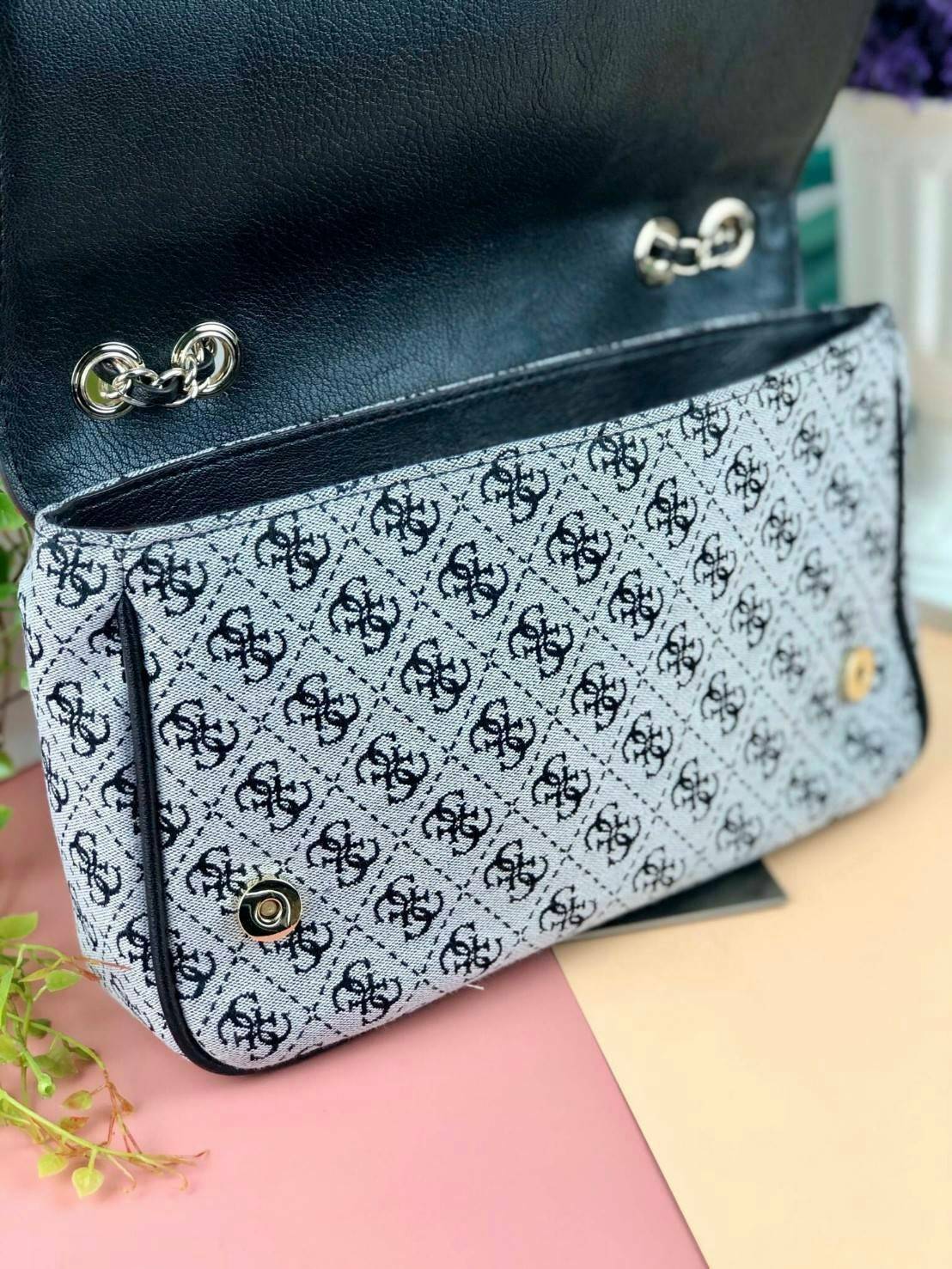 Guess Logo city handbag กระเป๋าสะพายไหล่ ตัวกระเป๋าเป็นผ้าลาย signature ของแบรนด์ ตัดกับหนังที่ตัวขอบกระเป๋า มาพร้อมพวงกุญแจโลโก้แบรนด์ ด้านหน้ามีโลโก้แบรนด์ ด้านหลังมีช่องใส่โทรศัพท์/บัตรได้ เปิดปิดแบบกระดุมแม่เหล็กซ้าย-ขวา ด้านในมีช่องซิป เล็ก 1 ช่อง แล