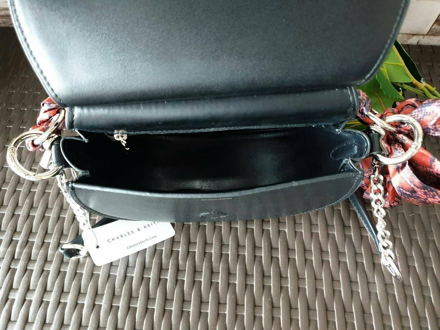 CHARLES & KEITH รุ่น LEATHER SATIN SCARF CROSSBODY BAG SL2-50150828 ราคาปกติช้อป ( ฿3,590.00 ) กระเป๋าถือ และ สะพาย ทรงโค้งมน หนังเรียบ ตั้งอยู่ทรง ด้านหน้าติดโลโก้แบรนด์ อะไหล่เงิน หูจับสายกระเป๋าร้อยเข้ากับห่วงเหล็กกลมๆ ด้วยผ้าลายสวยงามผูกเป็นโบว์เก๋ๆ ถ