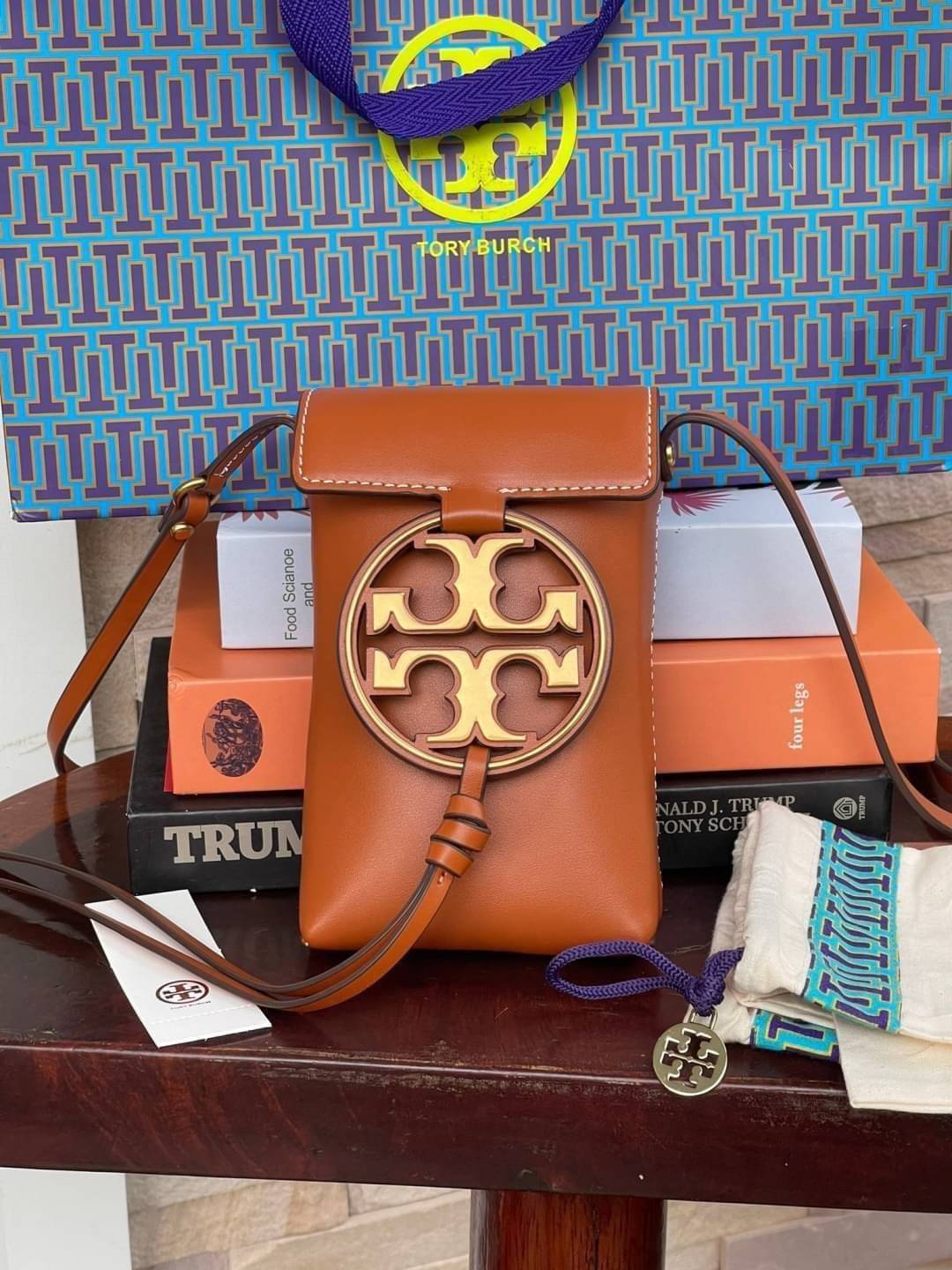 TORY BURCH MILLER METAL PHONE CROSSBODY อีกหนึ่งกระเป๋าใส่มือถือรุ่นฮิตที่เชื่อว่าหลาย ๆ คนต้องเคยเห็นผ่าน ๆ ตามาอย่างแน่นอน กับแบรนด์ Tory Burch ดีไซน์กระเป๋าทรงฝาพับแม่เหล็กใช้งานง่าย มาพร้อมดีเทล Logo แบรนด์โดดเด่นสีทองตัดกับหนังแกะสีดำ ดูหรูดูแพง! แต่