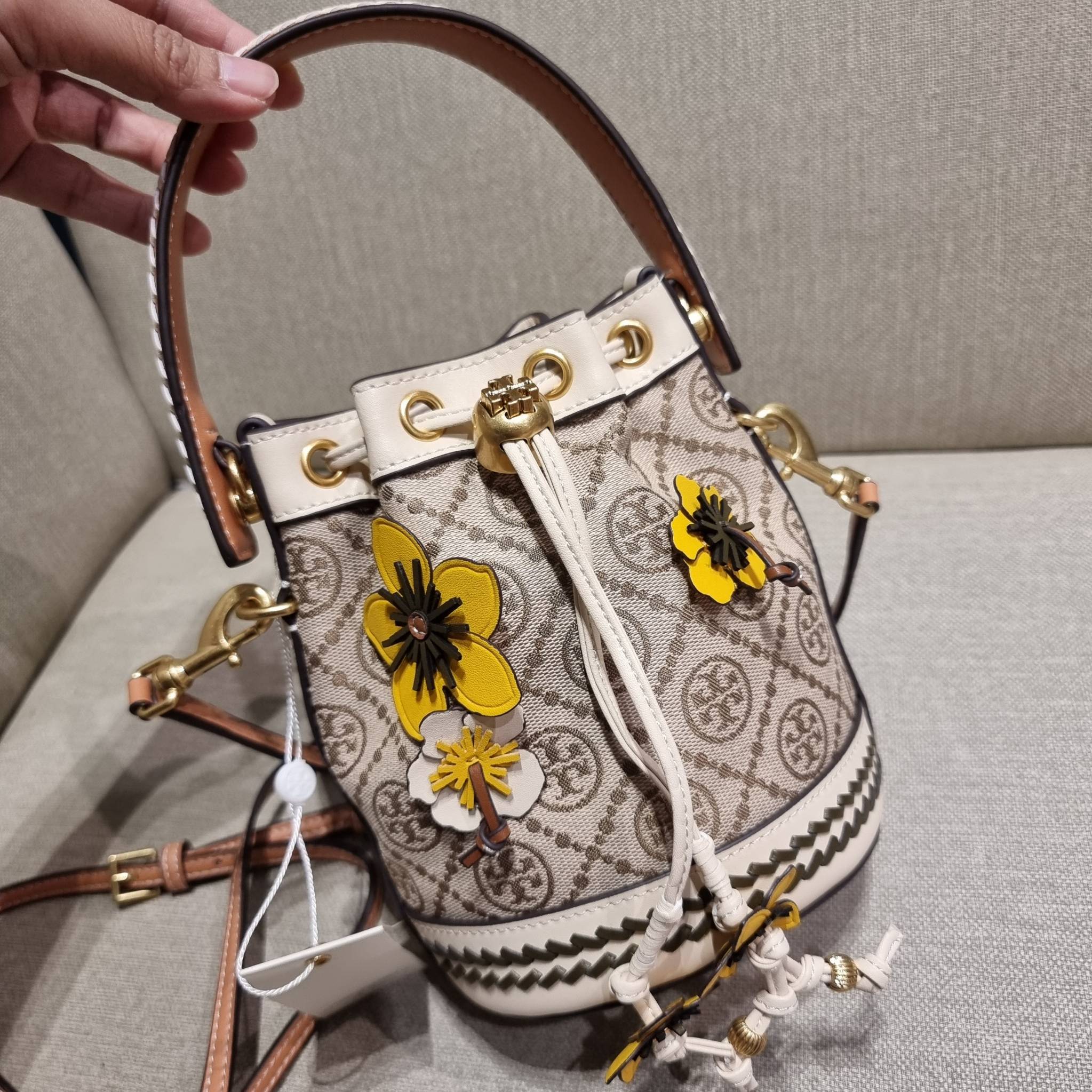 TORY BURCH MINI T MONOGRAM FLORAL BUCKET BAG คอลเลคชั่นใหม่ พร้อมเสิร์ฟความสวยให้ถึงบ้าน!! กระเป๋าบัคเก็ตทรงยอดนิยม ไซส์มินิ ดีไซน์ใหม่ล่าสุด สไตล์งานคราฟ มีลูกเล่นประดับดอกไม้กับตัวกระเป๋า และตัวรูดสาย วัสดุผ้า jacquard ตัดสลับหนังแท้ หูจับและขอบกระเป๋าต