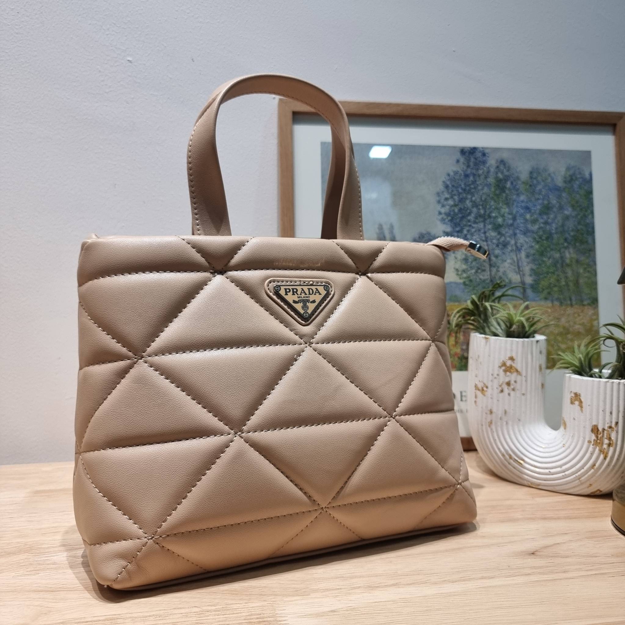 PRADA LEATHER PADDED BAG ใหม่ล่าสุด กับคอลเลคชั่นที่ทำออกมาตอบโจทย์ได้ทุกไลฟ์สไตล์ และเป็นยูนิเซ็กส์ กับกระเป๋าทรงโท้ท ขนาดกำลังดี วัสดุหนังเรียบ ตัดเย็บเดินเส้นลายตาราง ปากกระเป๋ามีซิปเปิดปิด ภายในเป็นช่องโล่ง