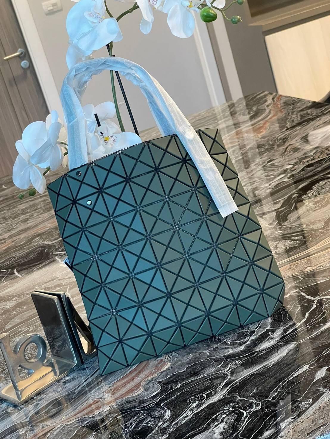 Baobao Issey Miyake Prism Kangaroo tote bag กระเป๋าถือทรงโท้ทที่ประดิษฐ์ขึ้นอย่างเชี่ยวชาญในญี่ปุ่น มาพร้อมแผงเรขาคณิตสำหรับการออกแบบที่ได้รับแรงบันดาลใจจากกระดาษพับ ซิลลูเอทอันเป็นเอกลักษณ์นี้ปิดท้ายด้วยสายรัดแบบอสมมาตร มีการพัฒนาโครงสร้างทรงสามเหลี่ยมเพ