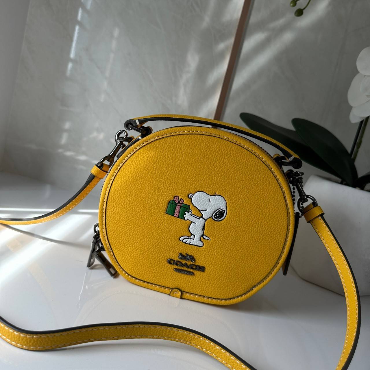 COACH X PEANUTS CANTEEN CROSSBODY WITH SNOOPY PRESENT MOTIF (CE845,CF290) กระเป๋าสะพายข้างทรงกลมไซส์มินิ มีหูจับ วัสหนังแท้ ด้านหน้าโดดเด่นด้วยรูปการ์ตูนSnoopy