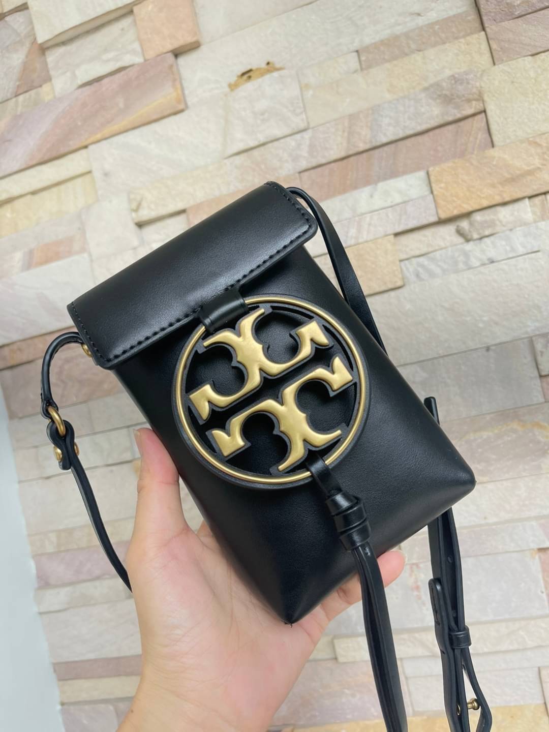 TORY BURCH MILLER METAL PHONE CROSSBODY อีกหนึ่งกระเป๋าใส่มือถือรุ่นฮิตที่เชื่อว่าหลาย ๆ คนต้องเคยเห็นผ่าน ๆ ตามาอย่างแน่นอน กับแบรนด์ Tory Burch ดีไซน์กระเป๋าทรงฝาพับแม่เหล็กใช้งานง่าย มาพร้อมดีเทล Logo แบรนด์โดดเด่นสีทองตัดกับหนังแกะสีดำ ดูหรูดูแพง! แต่