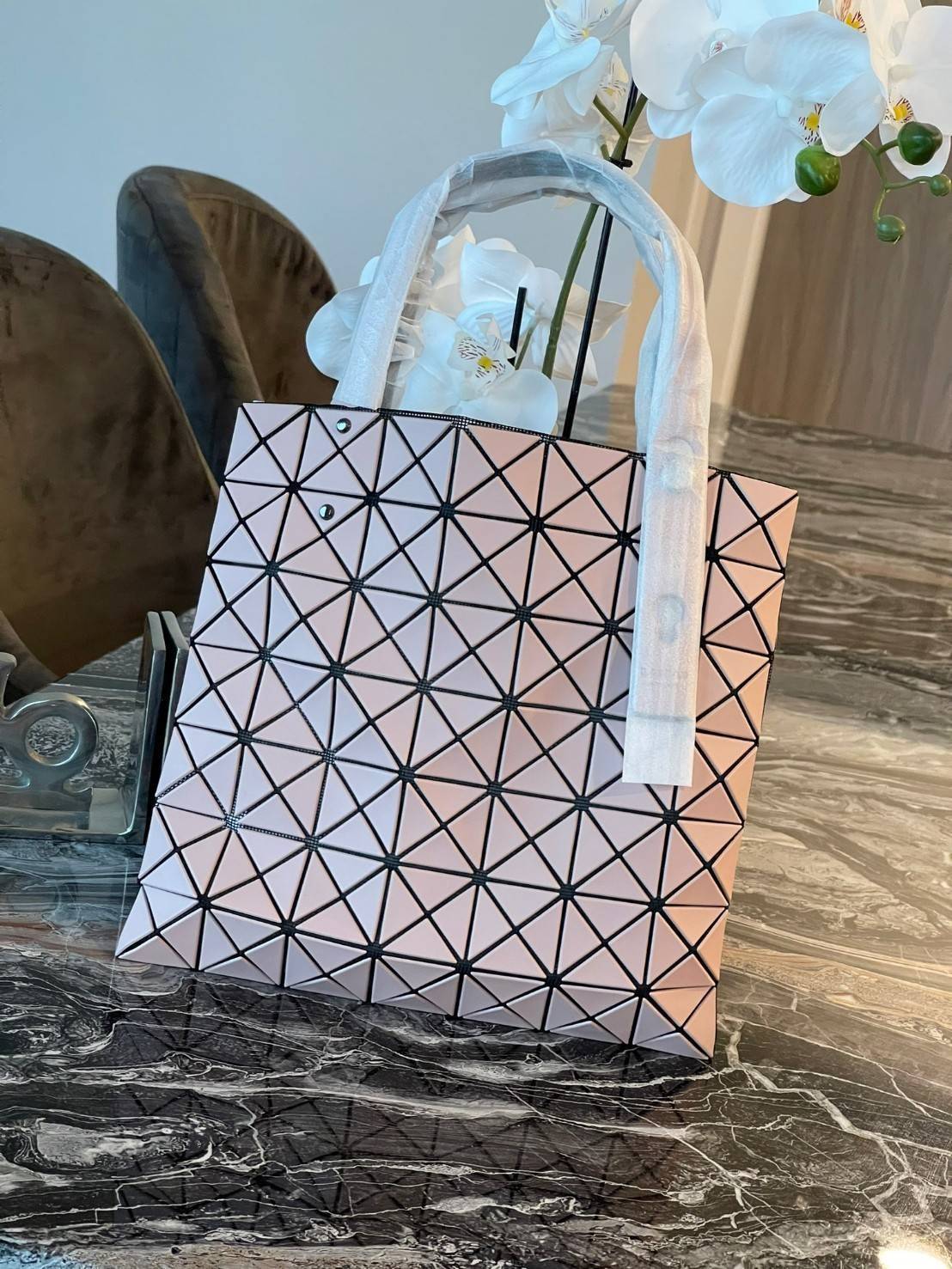 Baobao Issey Miyake Prism Kangaroo tote bag กระเป๋าถือทรงโท้ทที่ประดิษฐ์ขึ้นอย่างเชี่ยวชาญในญี่ปุ่น มาพร้อมแผงเรขาคณิตสำหรับการออกแบบที่ได้รับแรงบันดาลใจจากกระดาษพับ ซิลลูเอทอันเป็นเอกลักษณ์นี้ปิดท้ายด้วยสายรัดแบบอสมมาตร มีการพัฒนาโครงสร้างทรงสามเหลี่ยมเพ