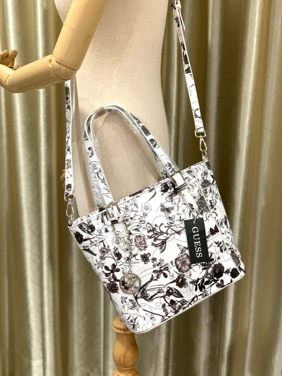 GUESS Women's Medium Floral Tote Bag กระเป๋าถือ คล้องไหล่หรือสะพาย ขนาดกลาง วัสดุหนังpu ลายดอกไม้ชนิดต่างๆรอบใบ เปิดปิดใช้งานด้วยซิปเดียวด้านบน ภายในมีกว้างใส่กระเป๋าสตาวค์ยาว มินิไอแพคได้ หูจับและสายสะพายปรับระดับได้ มาพร้อมกุญแจโลโก้guess สวยน่ารัก