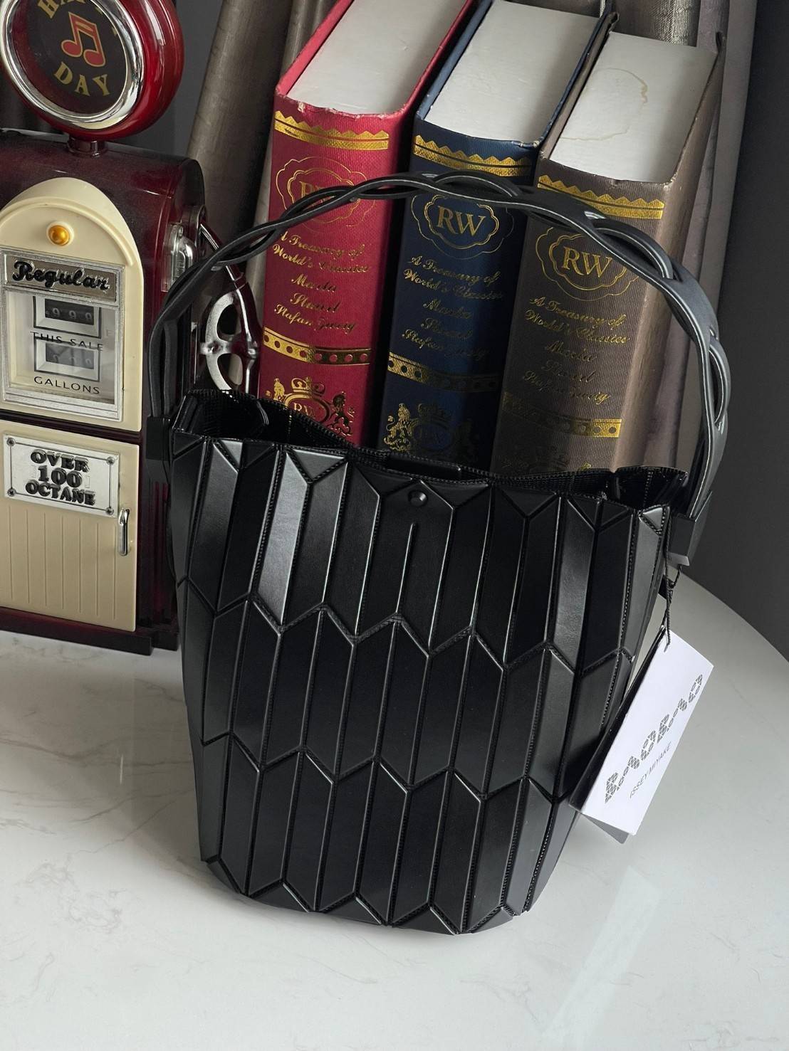 Small : BAO BAO ISSEY MIYAKE SMALL BUCKET เป็นกระเป๋าบัคเก็ตขนาดเล็กสามารถใช้ใส่กระเป๋าสตางค์และโทรศัพท์มือถือได้ ซีรีย์ใหม่นี้มีจุดเด่นที่แผ่นรูปทรงสี่เหลี่ยมด้านขนานในแนวตั้ง เกิดเป็นรูปทรงสามมิติซึ่งแตกต่างไปจากรูปทรงที่เกิดขึ้นจากแผ่นสามเหลี่ยม หูหิ้ว