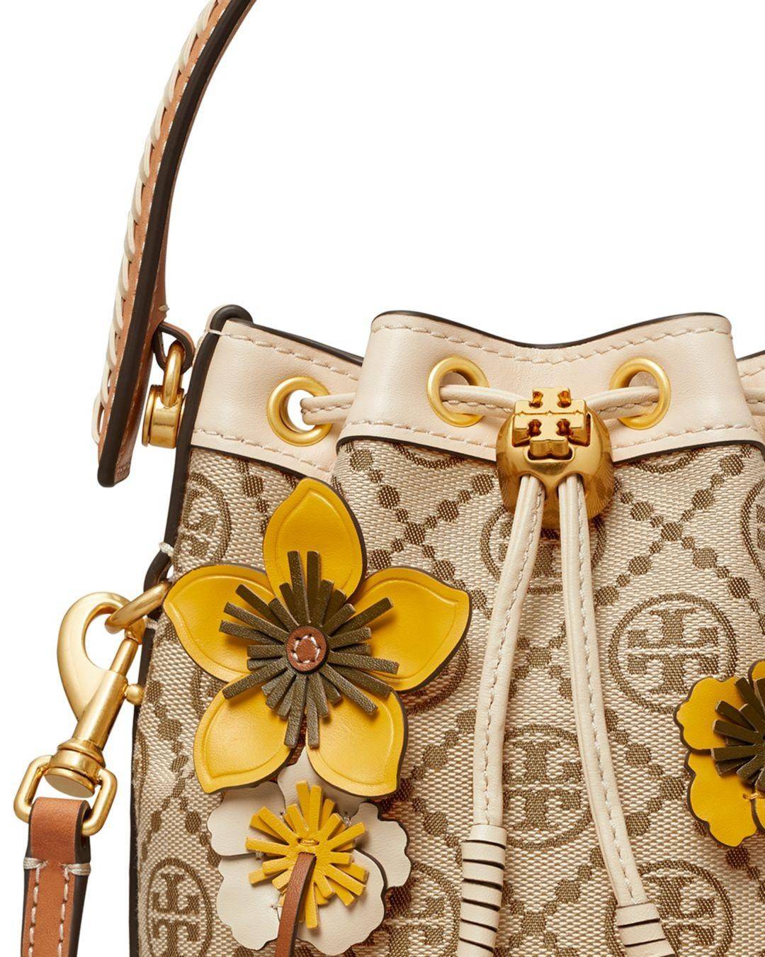TORY BURCH MINI T MONOGRAM FLORAL BUCKET BAG คอลเลคชั่นใหม่ พร้อมเสิร์ฟความสวยให้ถึงบ้าน!! กระเป๋าบัคเก็ตทรงยอดนิยม ไซส์มินิ ดีไซน์ใหม่ล่าสุด สไตล์งานคราฟ มีลูกเล่นประดับดอกไม้กับตัวกระเป๋า และตัวรูดสาย วัสดุผ้า jacquard ตัดสลับหนังแท้ หูจับและขอบกระเป๋าต