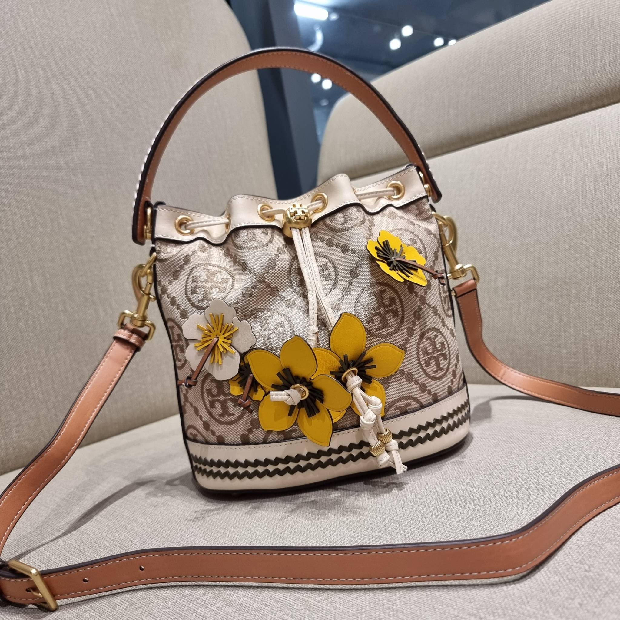 TORY BURCH T MONOGRAM FLORAL BUCKET BAG คอลเลคชั่นใหม่ พร้อมเสิร์ฟความสวยให้ถึงบ้าน!! กระเป๋าบัคเก็ตทรงยอดนิยม ดีไซน์ใหม่ล่าสุด สไตล์งานคราฟ มีลูกเล่นประดับดอกไม้กับตัวกระเป๋า และตัวรูดสาย วัสดุผ้า jacquard ตัดสลับหนังแท้ หูจับและขอบกระเป๋าตกแต่งลายสานสวย