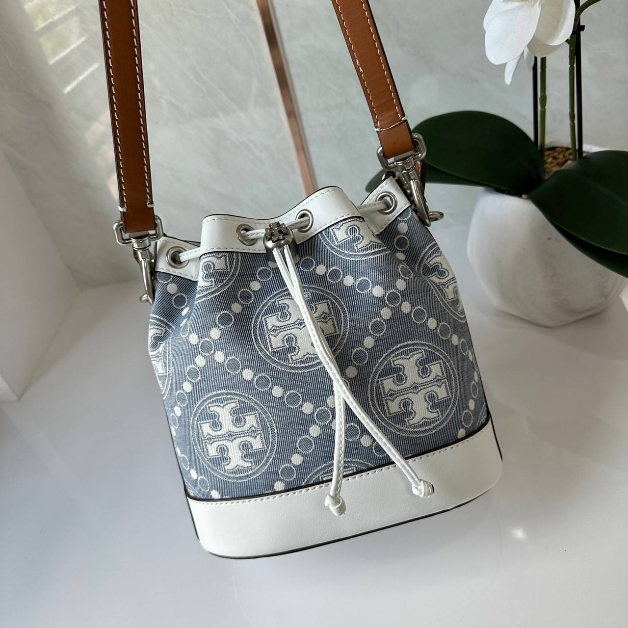TORY BURCH T Monogram Denim Bucket Bag MEDIUM คอลเลคชั่นใหม่ รูปแบบคลาสสิค พกพาความหรูหราไปได้ทุกที่ด้วยกระเป๋าทรง Bucket ขนาดกลางและปิดด้วยเชือกรูดพร้อมโลโก้แวววาว วัสดุผ้าเดนิมแจ็คการ์ด ตัดขอบหนังแท้