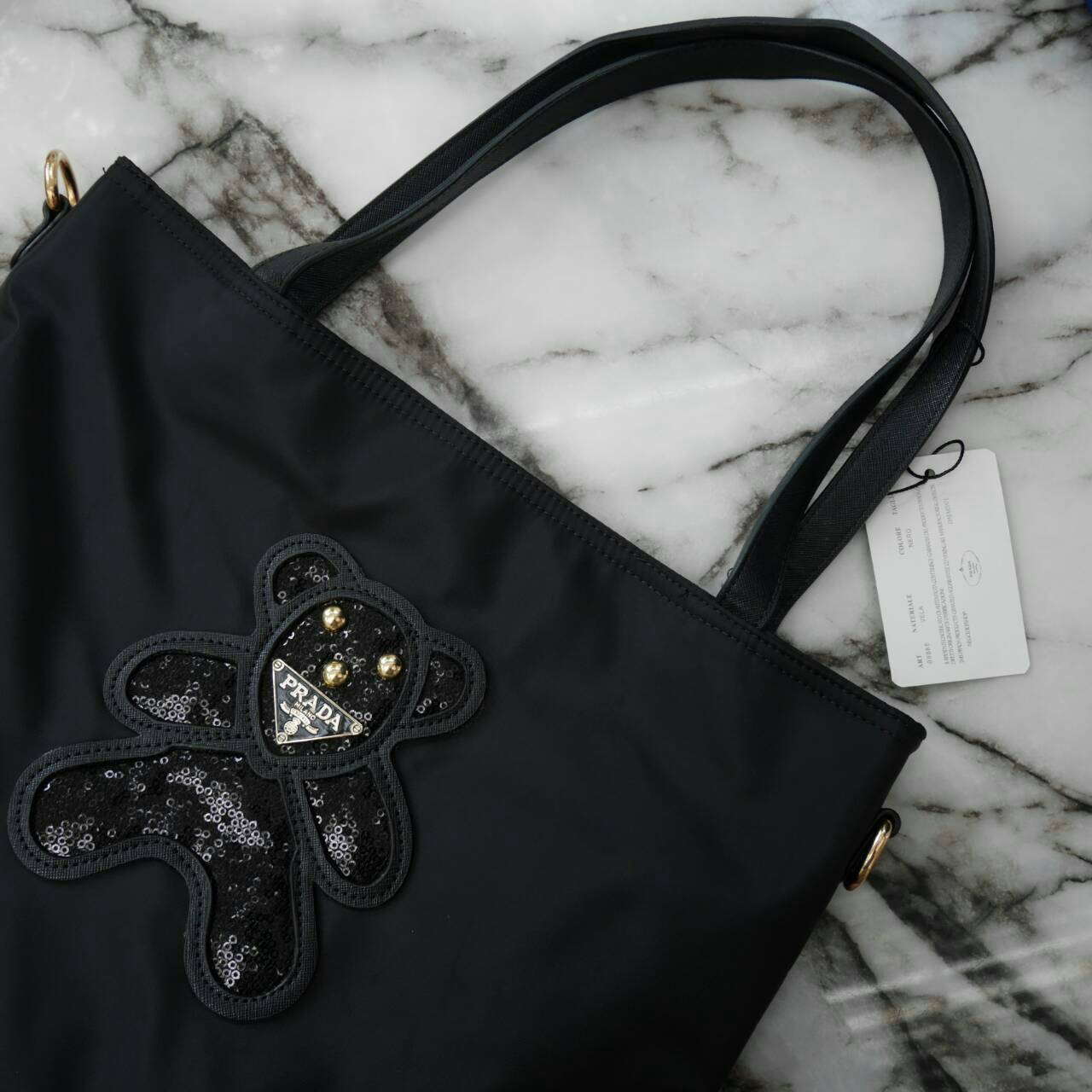 ReStock! งานขายดี ได้ กระเป๋าสะพายไหล่ ทรง TOTE จากแบรนด์ PRADA มาค่า เป็น กระเป๋าผ้าไนล่อน ตามแบบฉบับของแบรนด์เลย ใบนี้มีสายยาวให้ค่ะ สะพายเป็น shoulder bag หรือ ถือได้ค่ะ ด้านหน้าเป็นลายหมี ปักกลิ้ตเตอร์ +logo brand ใช้แล้วสวยมากๆ อะไหล่ทองหรูมาก จุของค