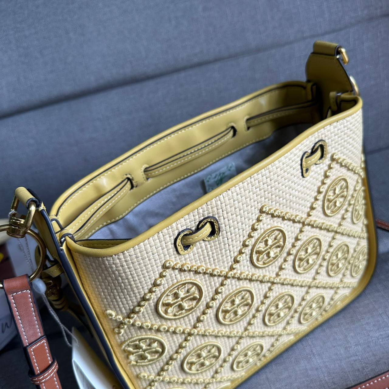 TORY BURCH T Monogram Straw Bell Bag กระเป๋าสะพายข้างรุ่นคลาสสิกที่ได้แรงบันดาลใจจากการควิลท์แบบดั้งเดิมของเพนซิลเวเนีย คอลเลกชันบ่งบอกถึงความมีสไตล์เหนือกาลเวลา รูปทรงเรียวโดดเด่น ปักทอลายแบรนด์อย่างสวยงาม เปิด ปิดด้วยเชือกรูด ด้านในช่องโล่งกว้าง ซับในผ้