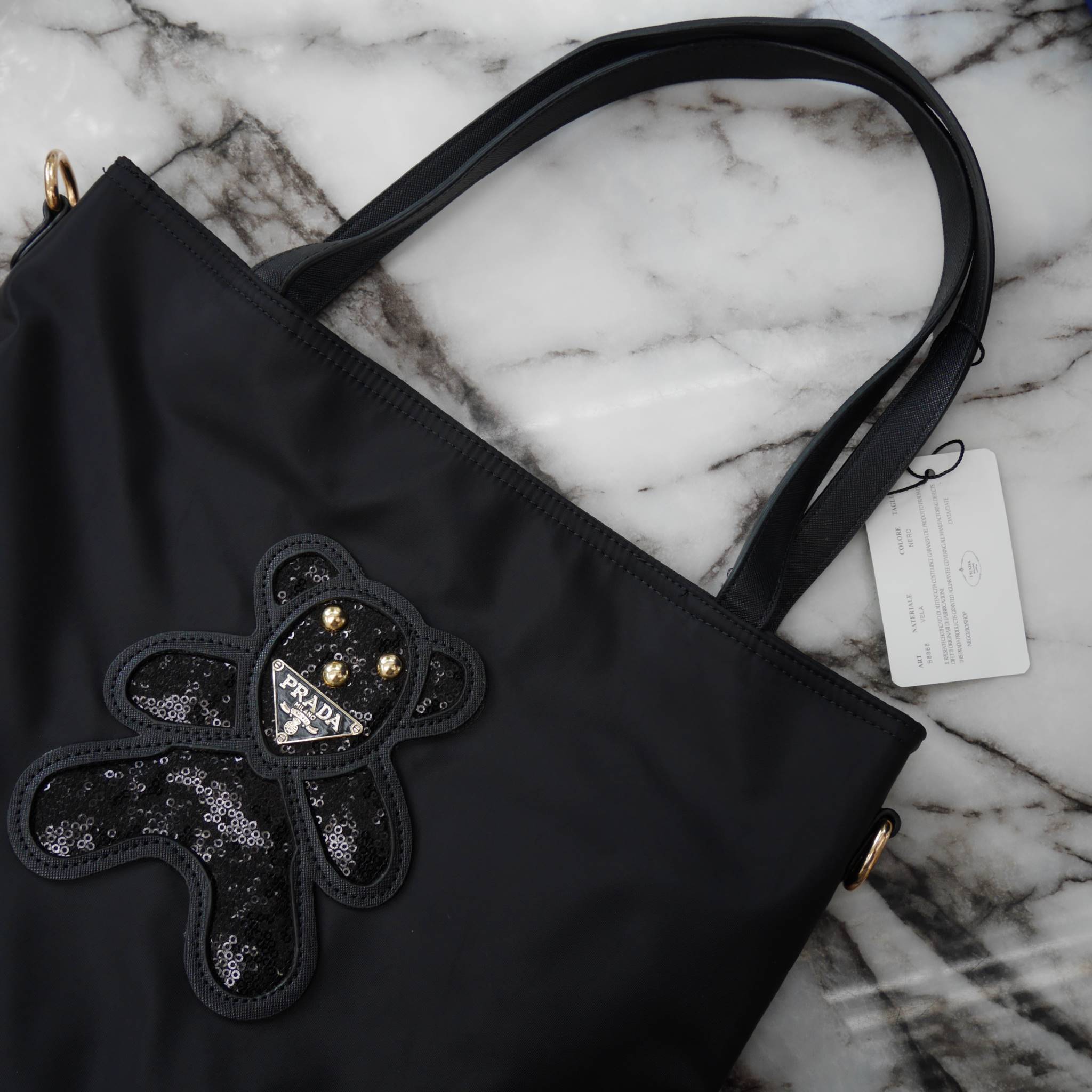 งานขายดีคะ ♡♡ กระเป๋าสะพาย ทรง TOTE จากแบรนด์ PRADA มาค่า ตัวกระเป๋าเป็น nylon ทั้งใบ สะพายเป็น shoulder bag หรือถือได้ค่ะ ด้านหน้าเป็นลายหมี ปักกลิ้ตเตอร์ + logo brand ใช้แล้วสวยมากๆ อะไหล่ทองหรูมาก จุของคุ้ม ใส่หนังสือ หรือ MacBook ได้ค้า 