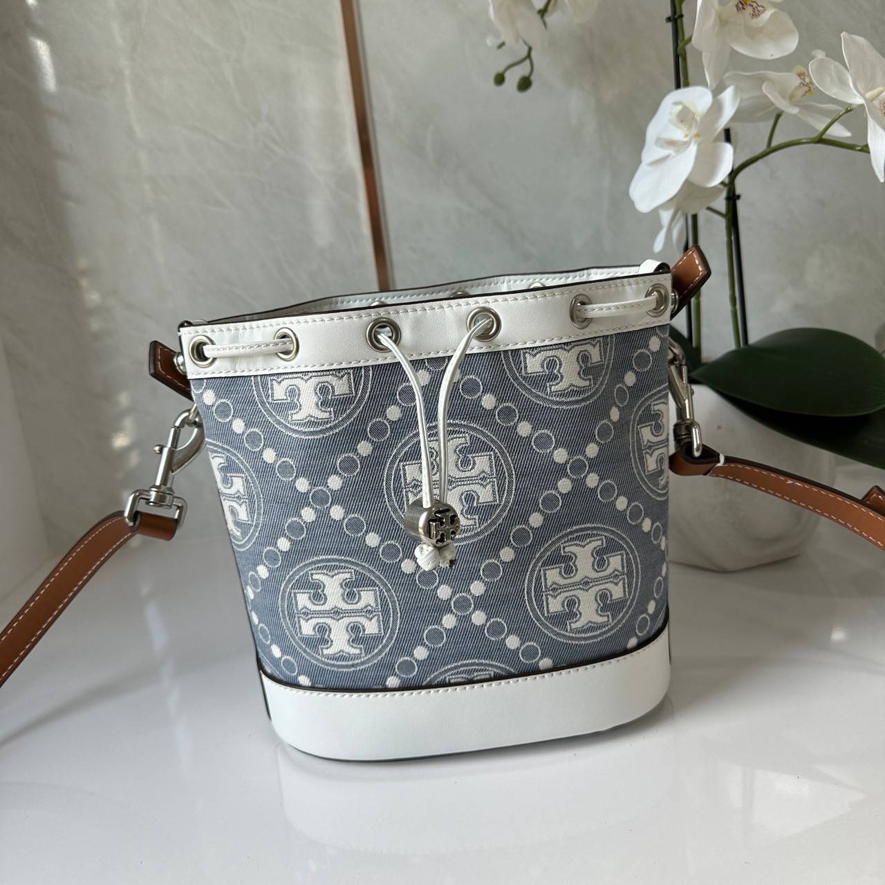 TORY BURCH T Monogram Denim Bucket Bag MEDIUM คอลเลคชั่นใหม่ รูปแบบคลาสสิค พกพาความหรูหราไปได้ทุกที่ด้วยกระเป๋าทรง Bucket ขนาดกลางและปิดด้วยเชือกรูดพร้อมโลโก้แวววาว วัสดุผ้าเดนิมแจ็คการ์ด ตัดขอบหนังแท้