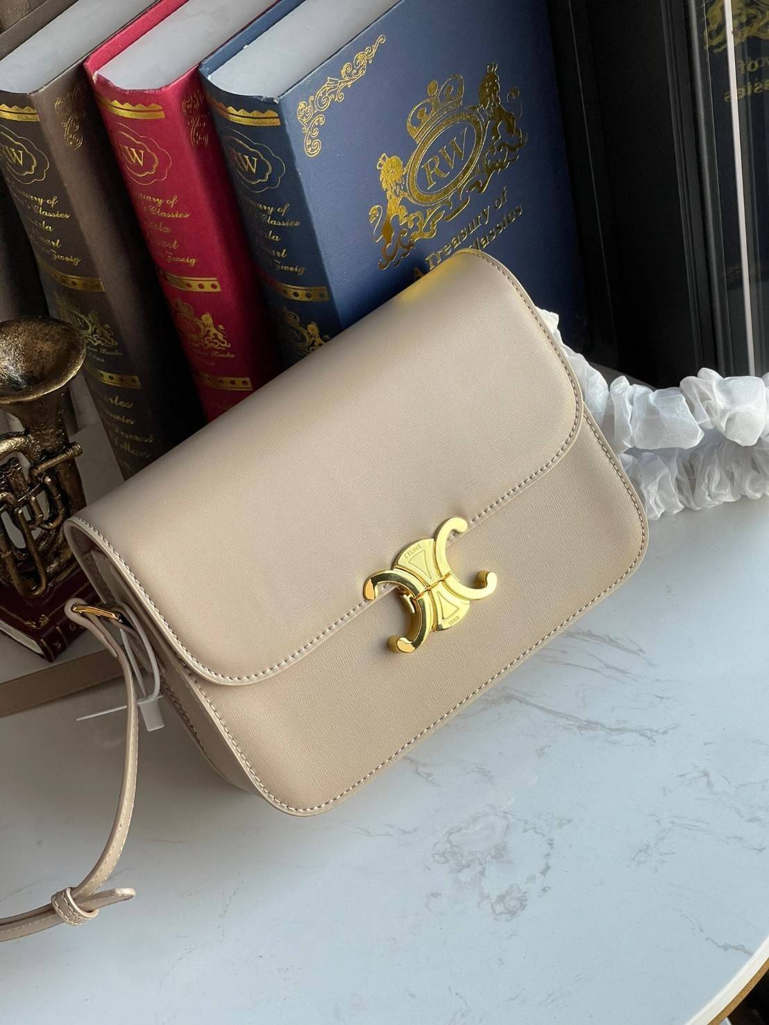 Celine MEDIUM TRIOMPHE BAG IN SHINY มีรูปทรงเป็นกล่องคล้ายกับกระเป๋า Classic Box แต่มีการออกแบบโลโก้ที่สะดุดตาแบบวินเทจ ด้วยดีไซน์ที่ดูโฉบเฉี่ยว แต่คงความคลาสสิคอย่างเต็มเปี่ยม ทำให้เป็นที่ดึงดูดความสนใจของสาวๆ สายสะพายสามารถปรับระดับได้ มีความคล่องตัวในก